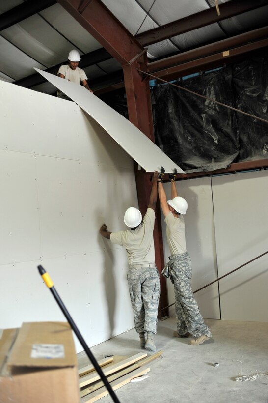 Staff Sgt. Christopher Shivers and Senior Airman Timothy Poole, 316th Civil Engineering Squadron structural technicians, lift a sheet of drywall up to Airman 1st Class Herson Leron, 316 CES structural technician, during a restoration of the Honor Guard building at Joint Base Andrews, Md.  June 22, 2010. The base honor guard is having its ceremonial hangar redone, and provides the 316 CES hands-on experience with remodeling a major project. (U.S. Air Force photo by Staff Sgt. Renae Saylock)