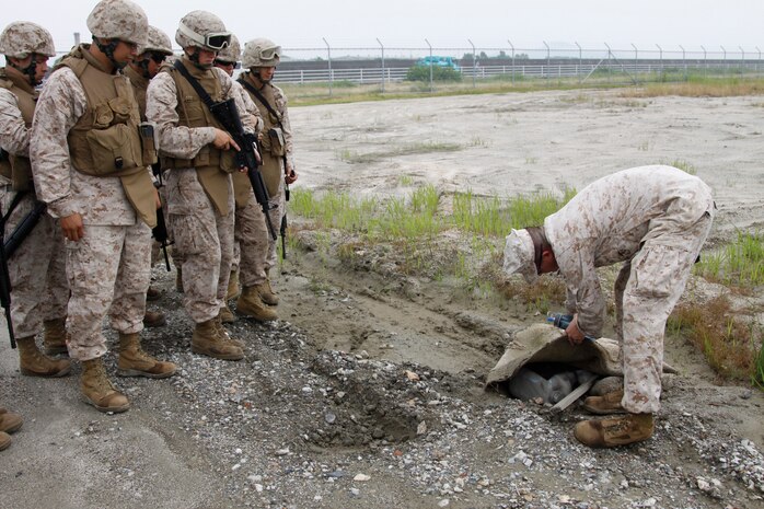 Marine Wing Support Squadron 171 Marines look on as Sgt. Ryan Wilhite, a Marine Wing Support Squadron 171 explosive ordnance disposal assistant team leader, explains what to look for when looking for improvised explosive devises during an IED training course conducted at the north side dump here June 23. The IED course included a motor transport course and a foot patrol during which Marines had to successfully identify and avoid IEDs.
