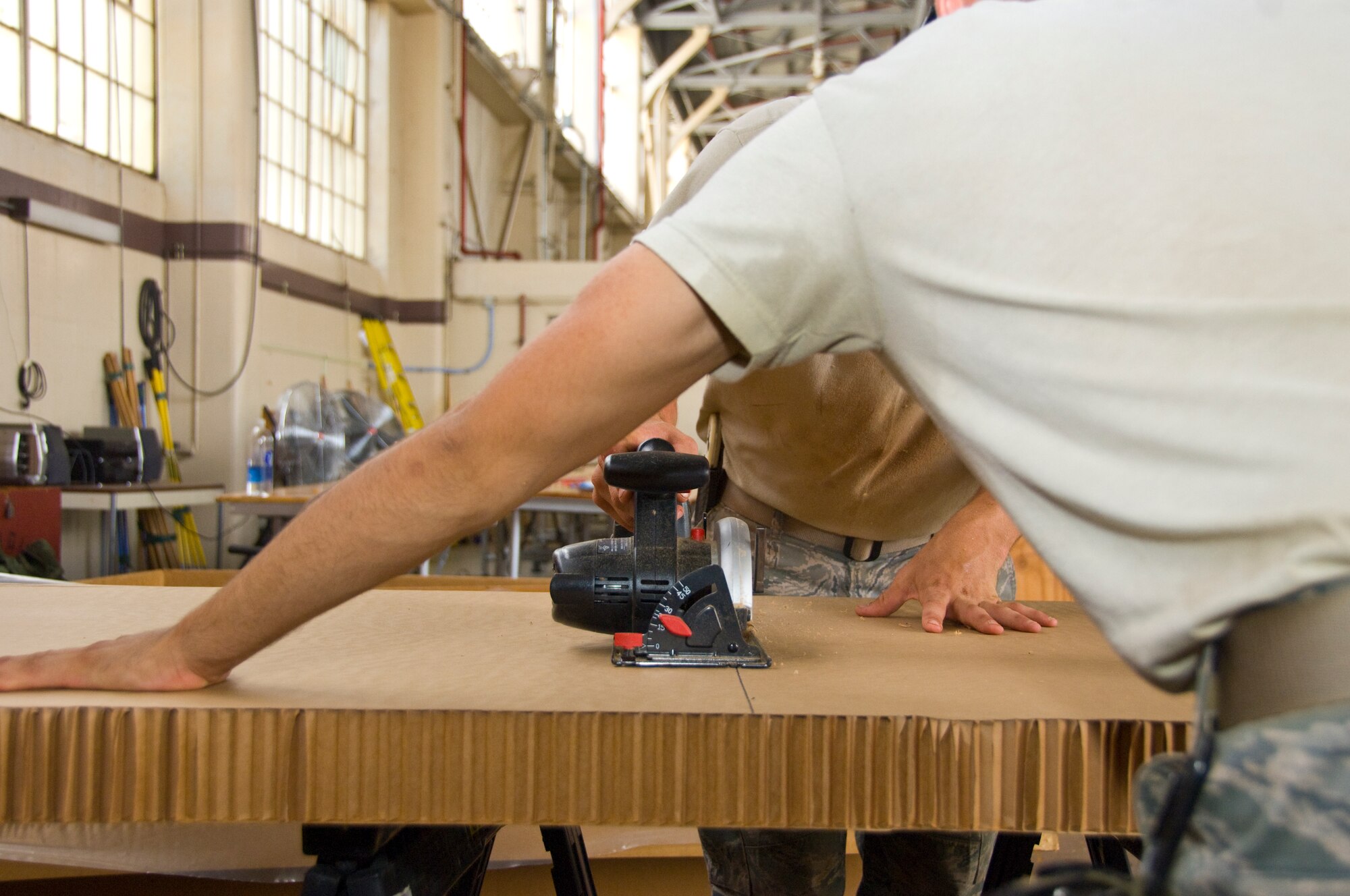 Senior Airman Alejandro Ramos, 647th Logistics Readiness Squadron air transportation specialist, braces a piece of cardboard as Airman 1st Class Sean Cyphert, 647th LRS air transportation specialist, cuts it with a saw at Hangar 7 June 18. The cardboard was used in a pallet built to deliver  food through airdrop to Marines and Seabees on the island of Hawaii as part of the Rim of the Pacific exercise. (U.S. Air Force photo by Staff Sgt. Nathan Allen)