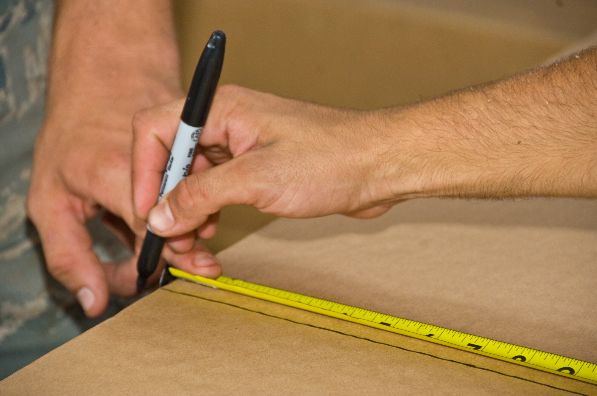 Senior Airman Alejandro Ramos, 647th Logistics Readiness Squadron air transportation specialist, holds a piece of cardboard steady as Senior Airman Micah Smith, 647th LRS air transportation specialist, marks it with a sharpie at Hangar 7 June 18. The cardboard was used in a pallet built to deliver  food through airdrop to Marines and Seabees on the island of Hawaii as part of the Rim of the Pacific exercise. (U.S. Air Force photo by Staff Sgt. Nathan Allen)