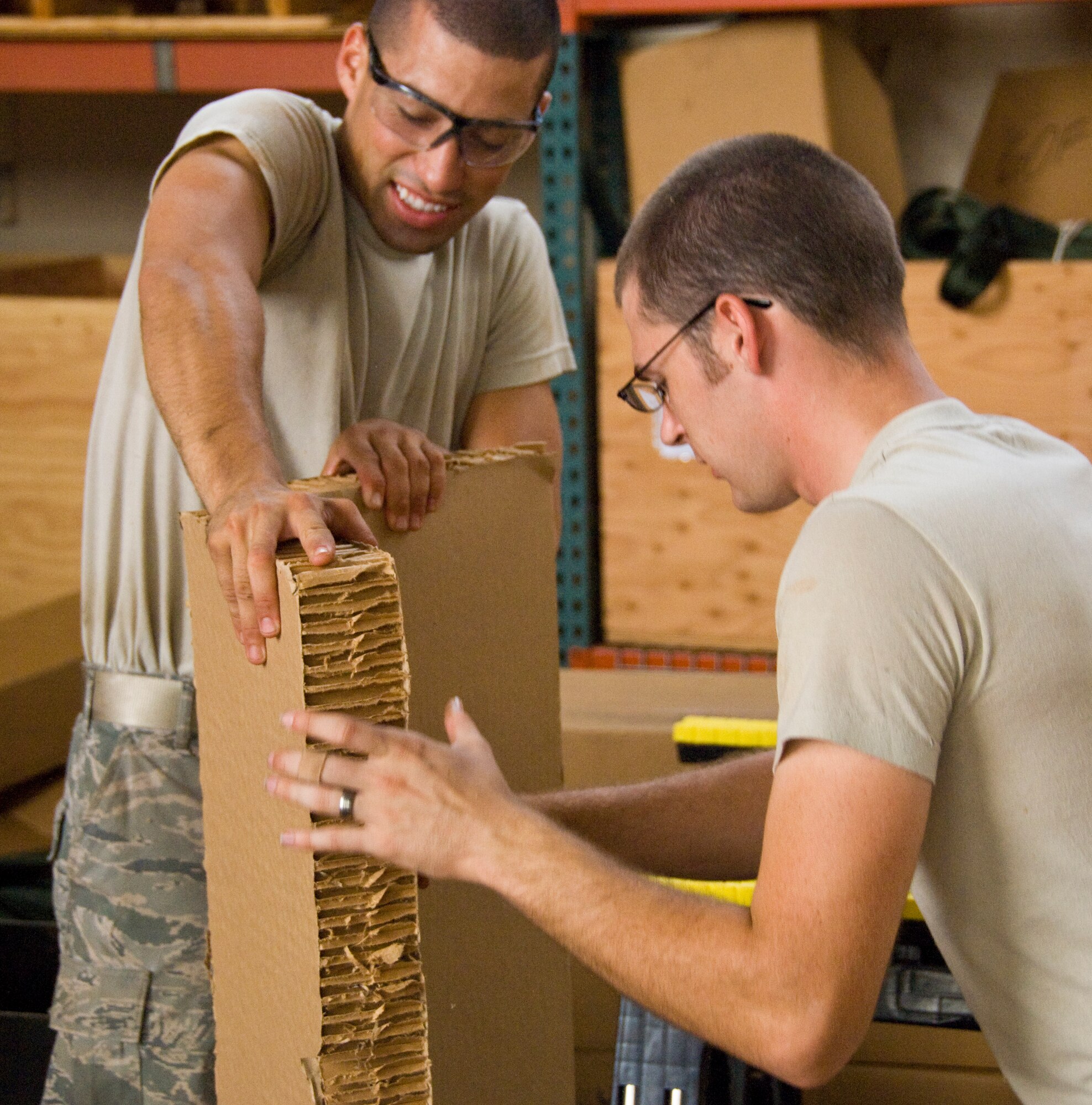 Senior Airman Alejandro Ramos, 647th Logistics Readiness Squadron air transportation specialist, braces a piece of cardboard as Senior Airman Micah Smith, 647th LRS air transportation specialist, slices it with a box cutter at Hangar 7 June 18. The cardboard was used in a pallet built to deliver  food through airdrop to Marines and Seabees on the island of Hawaii as part of the Rim of the Pacific exercise. (U.S. Air Force photo by Staff Sgt. Nathan Allen)