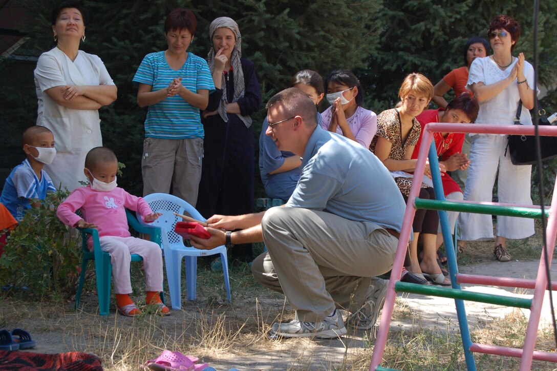 Staff Sgt. Daniel Stone of the U.S. Air Forces Central band "Sirocco" entices a bashful young patient into playing an instrument during a performance at the children’s cancer center in the Kyrgyz Republic Capital of Bishkek. The band was on a ten day tour at Manas AB where they played at schools, villages, orphanages, the U.S. Embassy and at the base.