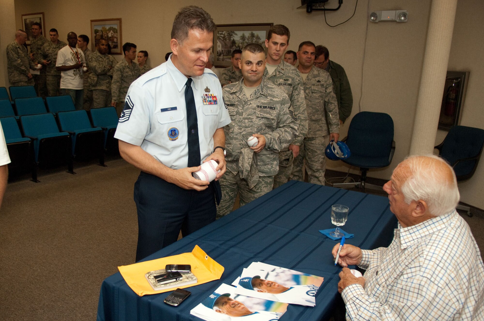 HANSCOM AIR FORCE BASE, Mass. - Tommy Lasorda (sitting), hall-of-fame baseball pitcher and manager, signs a baseball and chats with Senior Master Sgt. Clarence Yoh following Lasorda’s speech to Airmen and civilians at the Hanscom Conference Center on June 18. (U.S. Air Force photo by Rick Berry)