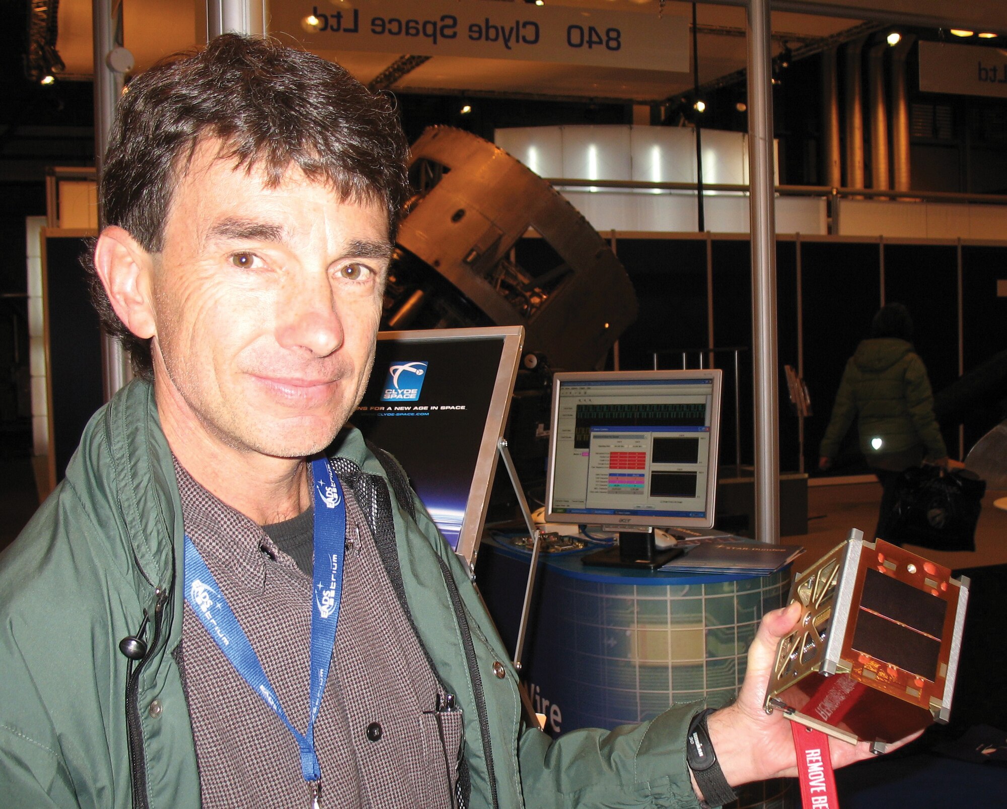 ASTRIA staff attending the International Astronautical Congress (Glasgow, Scotland) demonstrate a 'cubesatellite' (10 cm on each side) that presents unique space tracking challenges due to its small size. 
(Image provided by Dr. Moriba Jah, AFRL/RDSM)
