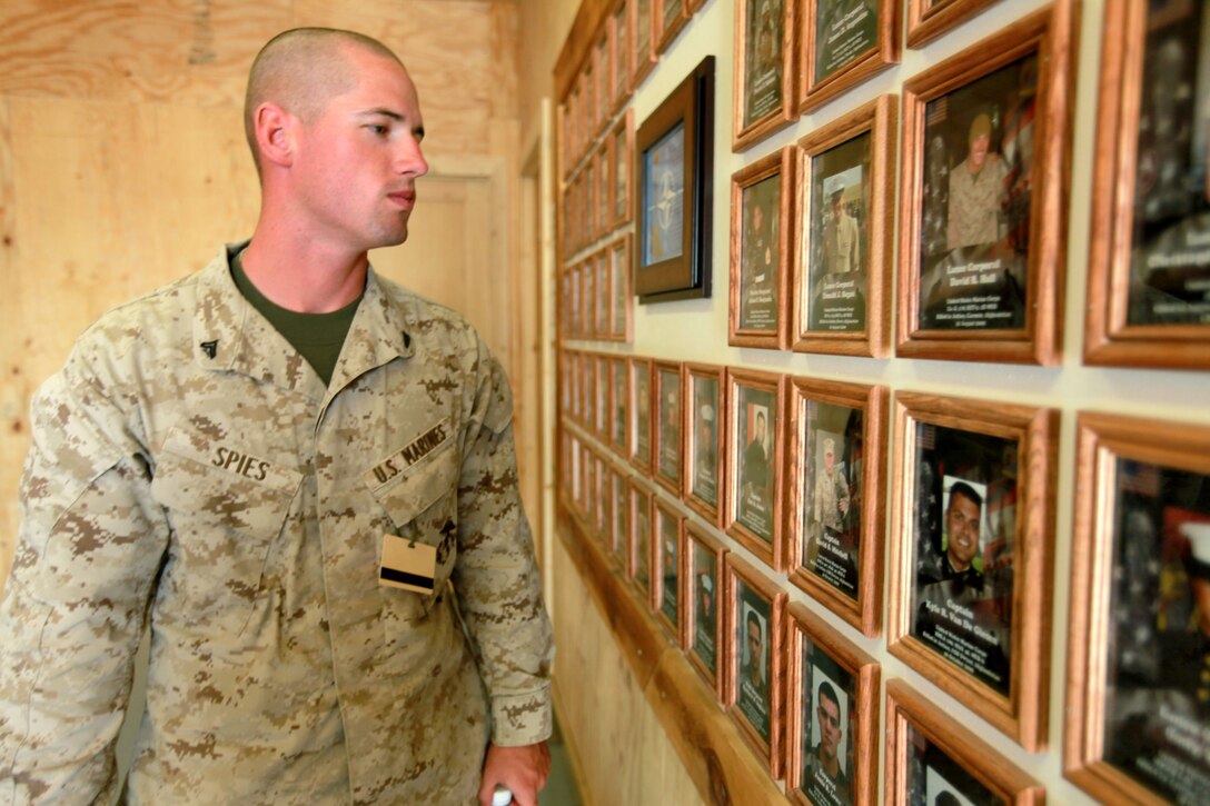 Corporal Paul A. Spies, 23, from Corvallis, Ore., a combat engineer with Alpha Company, 9th Engineer Support Battalion, 1st Marine Logistics Group (Forward), glances at a wall adorned with framed photos of fallen brethren at the Regional Command Southwest headquarters building at Camp Leatherneck, Afghanistan, June 23. Spies is the brainchild of the ‘Afghan Adopt a Road Initiative,’ an initiative that, if approved, could help counter the number one threat to coalition forces – IEDs. In exchange for Afghan villagers helping to reduce or eliminate IEDs on their roads, they would receive incentives such as medical and dental care, as well as infrastructure support in the form of schools, wells and irrigation. Upon further review, commanders will decide whether or not to launch the AARI program.