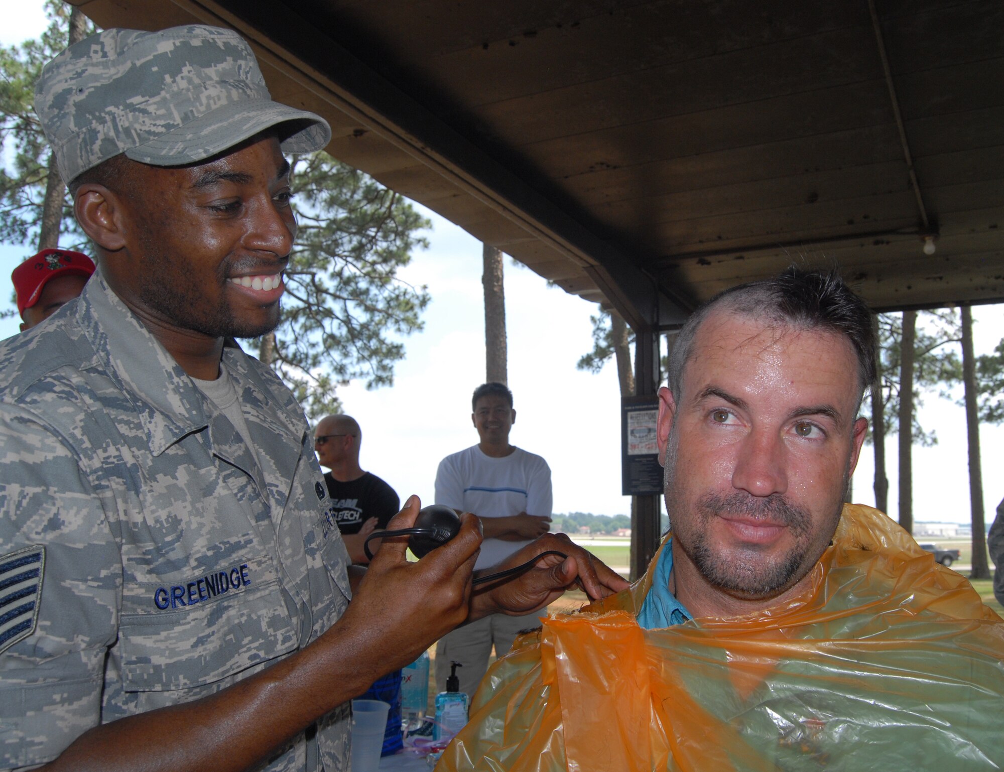 Tech. Sgt. Kareem Greenidge (left), 3rd Aerial Port Squadron, shaves the head of Edwin Byrnes, 3rd APS assistant director of operations during a squadron picnic June 25 at Woodland Park, here. Mr. Byrnes, Lt. Col. Frank Flores, 3rd APS commander, and Chief Scales and agreed to shave their heads provided the squadron scored an "outstanding” in a recent inspection. (U.S. Photo/ 1st Lt. Cammie Quinn) 