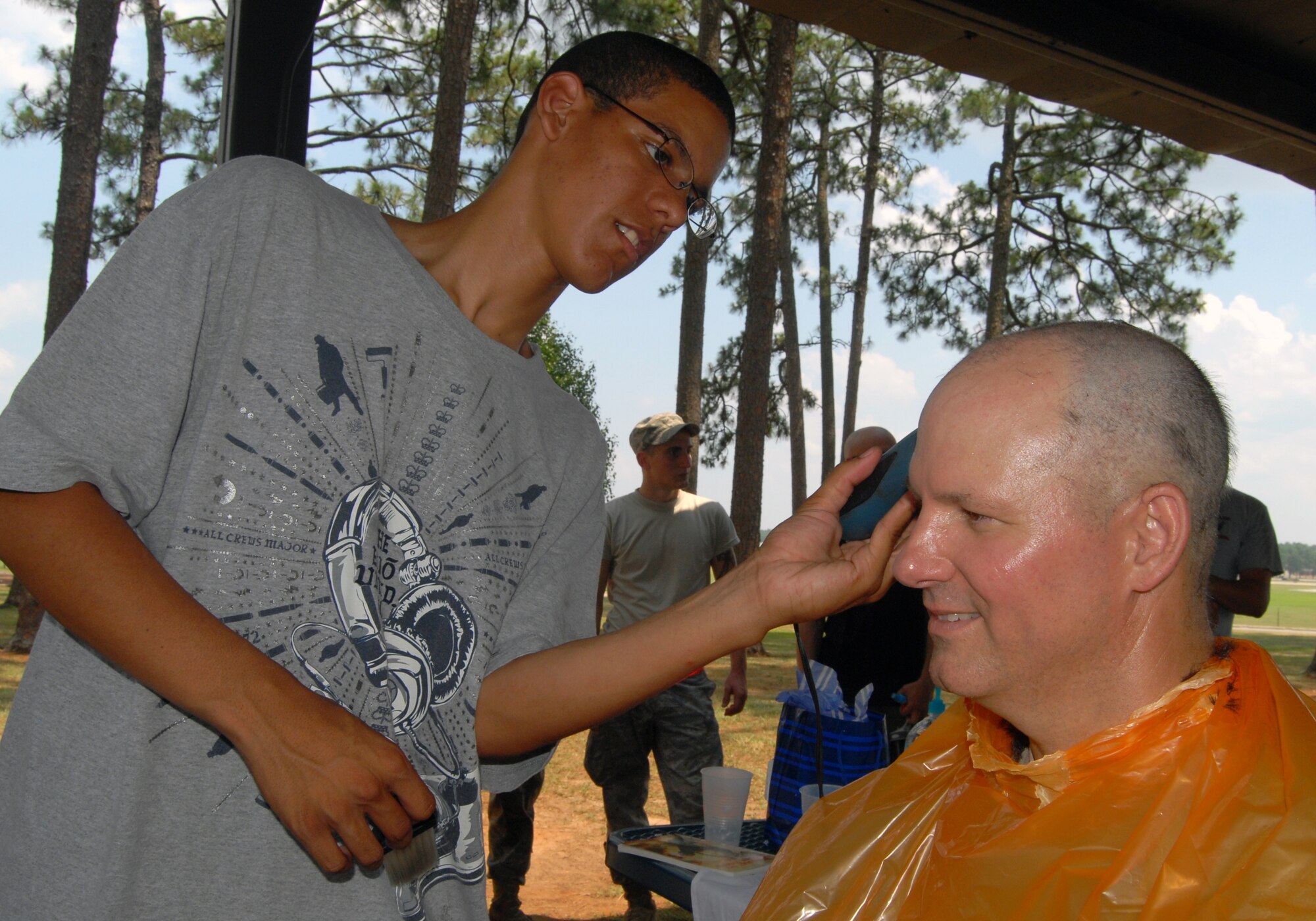 Airmen 1st Class Gregory Butler (left), 3rd Aerial Port Squadron, shaves the head of Chief Master Sgt. Patton Scales, 3rd APS superintendent, during a squadron picnic June 25 at Woodland Park. Chief Scales, Lt. Col. Frank Flores, 3rd APS commander, and Edwin Byrnes, 3rd APS assistant director of operations, agreed to shave their heads provided the squadron scored an "outstanding” in a recent inspection. (U.S. Photo/ 1st Lt. Cammie Quinn)