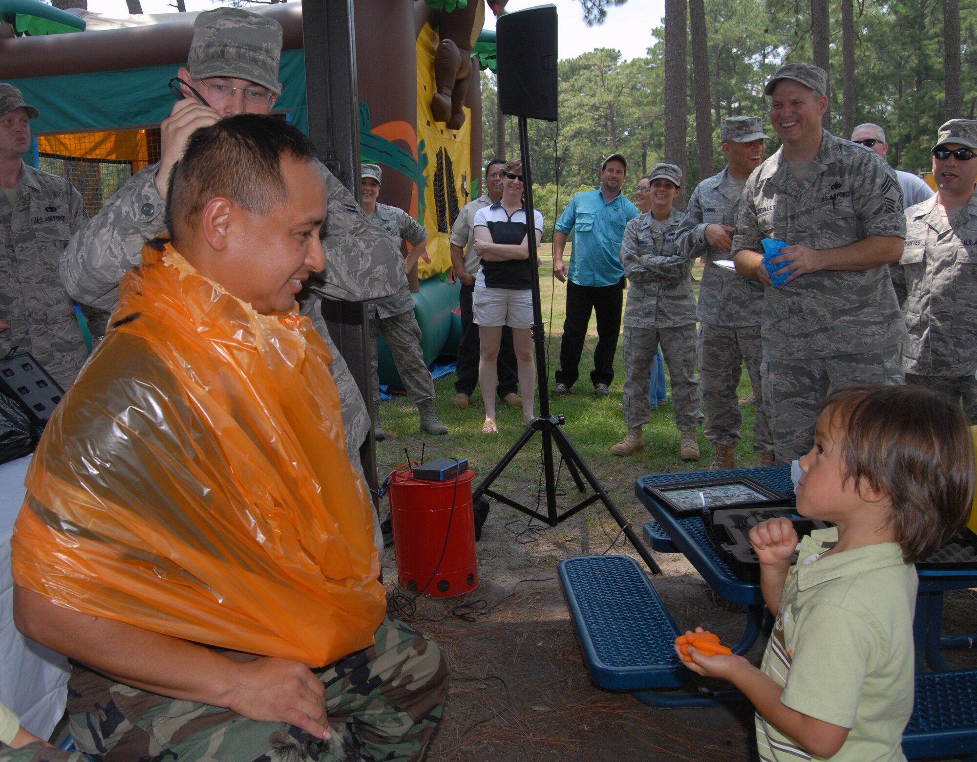 Airman 1st Class Mitchell Bordley, 3rd Aerial Port Squadron, shaves the head of Lt. Col. Frank Flores’, 3rd APS commander, while son Luca Flores, watches during a squadron picnic June 25 at Woodland Park. Colonel Flores, Chief Master Sgt. Patton Scales, 3rd APS superintendent and Edwin Byrnes, 3rd APS assistant director of operations, agreed to shave their heads provided the squadron scored an "outstanding” in a recent inspection. (U.S. Photo/ 1st Lt. Cammie Quinn)