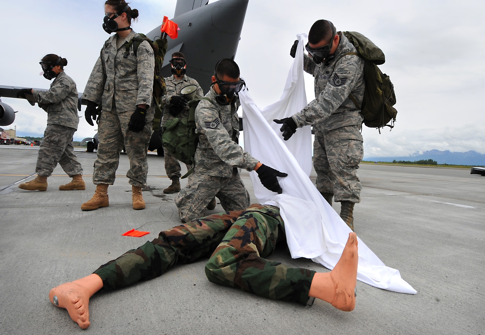 Members of the 3rd Force Support Squadron's search and recovery team cover a manikin that simulates a dead body found at the accident scene during the emergency management exercise at Joint Base Elmendorf-Richardson, June 29. During the search and recovery portion of an exercise, players practice searching and recording human remains or belongings after an accident. (Air Force photo by Senior Airman Cynthia Spalding)