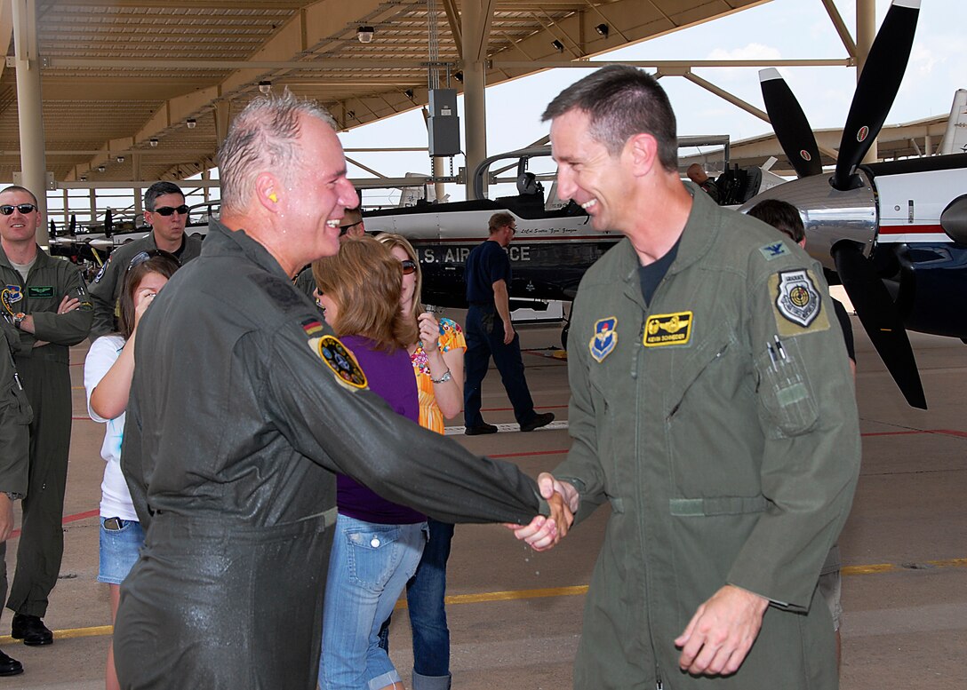 Col. Kevin Schneider, 80th Flying Training Wing commander (right), congratulates German air force Col. Axel Pohlmann, outgoing 80th Operations Group commander, following the tradition of friends and family drenching the outgoing pilot with water after landing his final flight June 24, 2010. Colonel Pohlmann will become the senior international representative and chief of plans for the Combined Air Operations Center in Uedem, Germany. (U.S. Air Force Photo/Harry Tonemah)