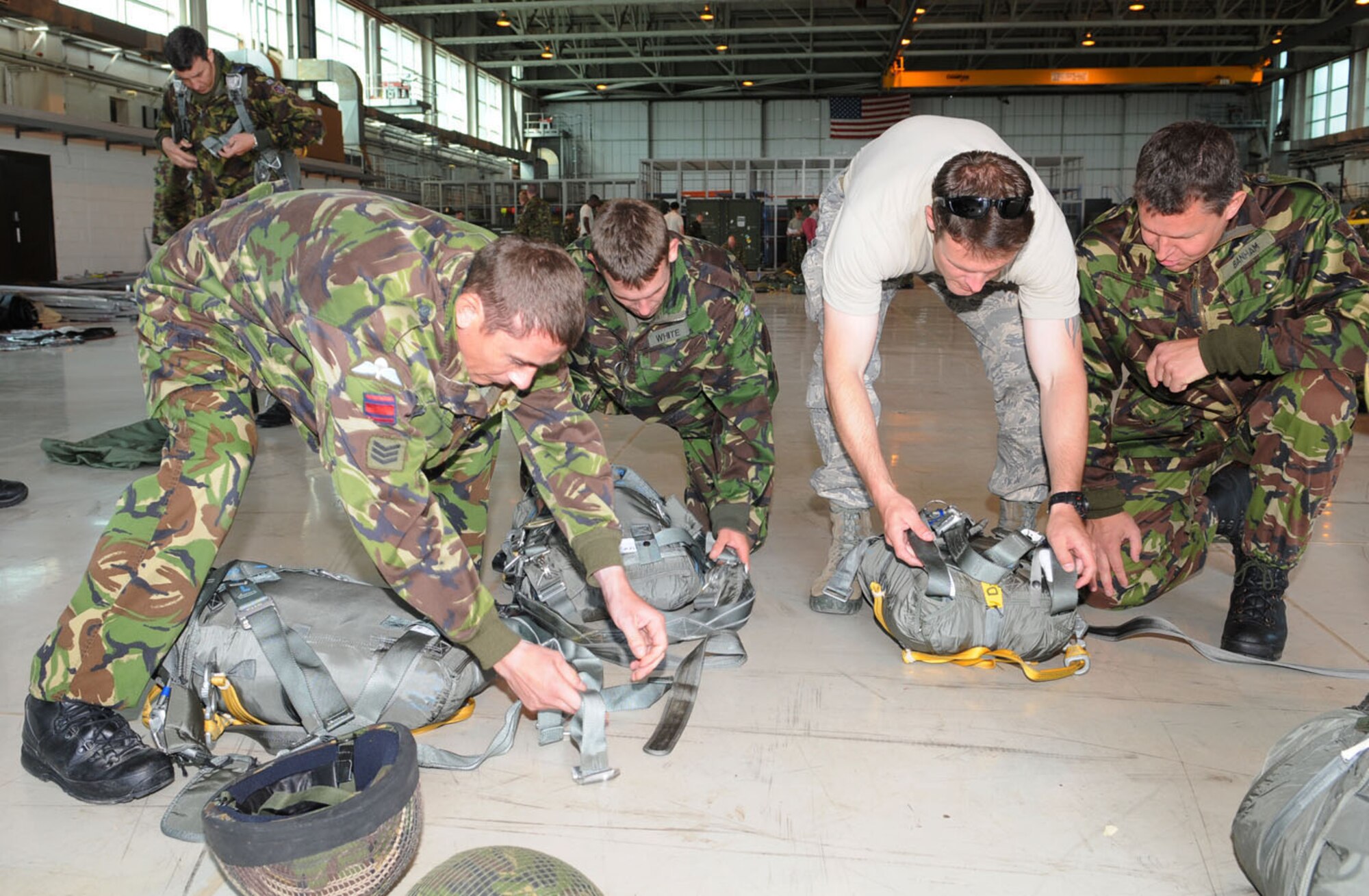 Staff Sgt. Kendrick Passey, second right, 321st Special Tactics Squadron, helps members from the 23 Engineer Regiment, Woodbridge, Suffolk, check straps of the parachutes they were using to do a jump from one of the U.S. Air Force's MC-130H aircraft June 22. The British military members were at RAF Mildenhall to earn their American jump wings, so they used parachutes belonging to the 321st STS, and jumped with Airmen from the 7th Special Operations Squadron. (U.S. Air Force photo/Karen Abeyasekere)