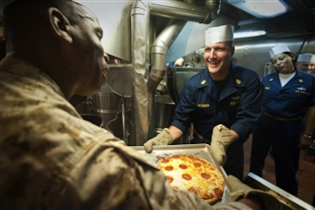 U.S. Navy Chief Petty Officer Chris Sherman hands a tray of pizzas to U.S. Marine Corps Master Gunnery Sgt. Erik Jackson while they and other senior enlisted sailors and Marines are aboard the USS New Orleans at sea in the Pacific Ocean, June 26, 2010. Sherman is assigned to Amphibious Squadron 5.