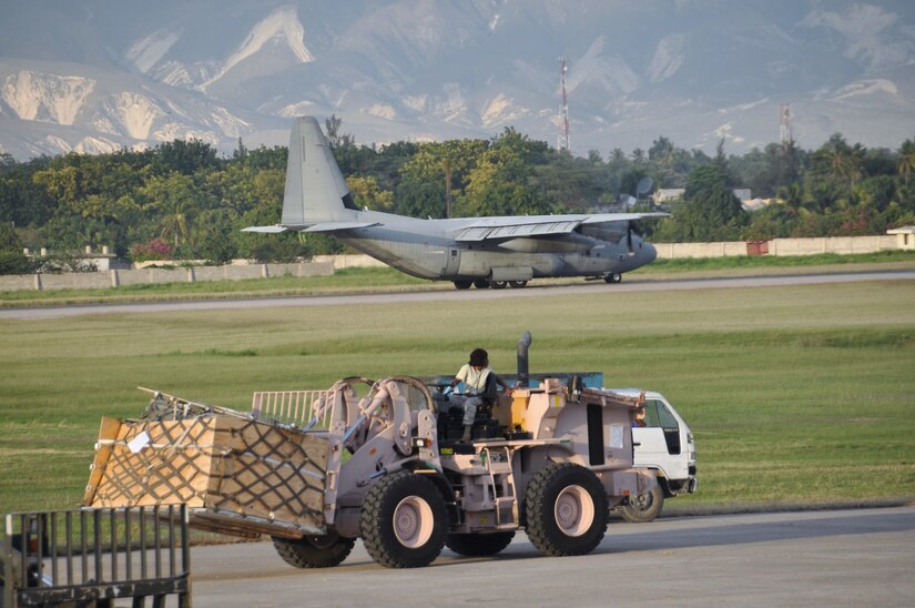 A C-130 Hercules lands behind an Airman unloading cargo with a 10K forklift at Toussaint Louverture International Airport in Haiti.  Aerial porters from the 621st Contingency Response Wing handled approximately 1 million lbs of cargo a day throughout the deployment. (U.S Air Force photo/Capt. Dustin Doyle)