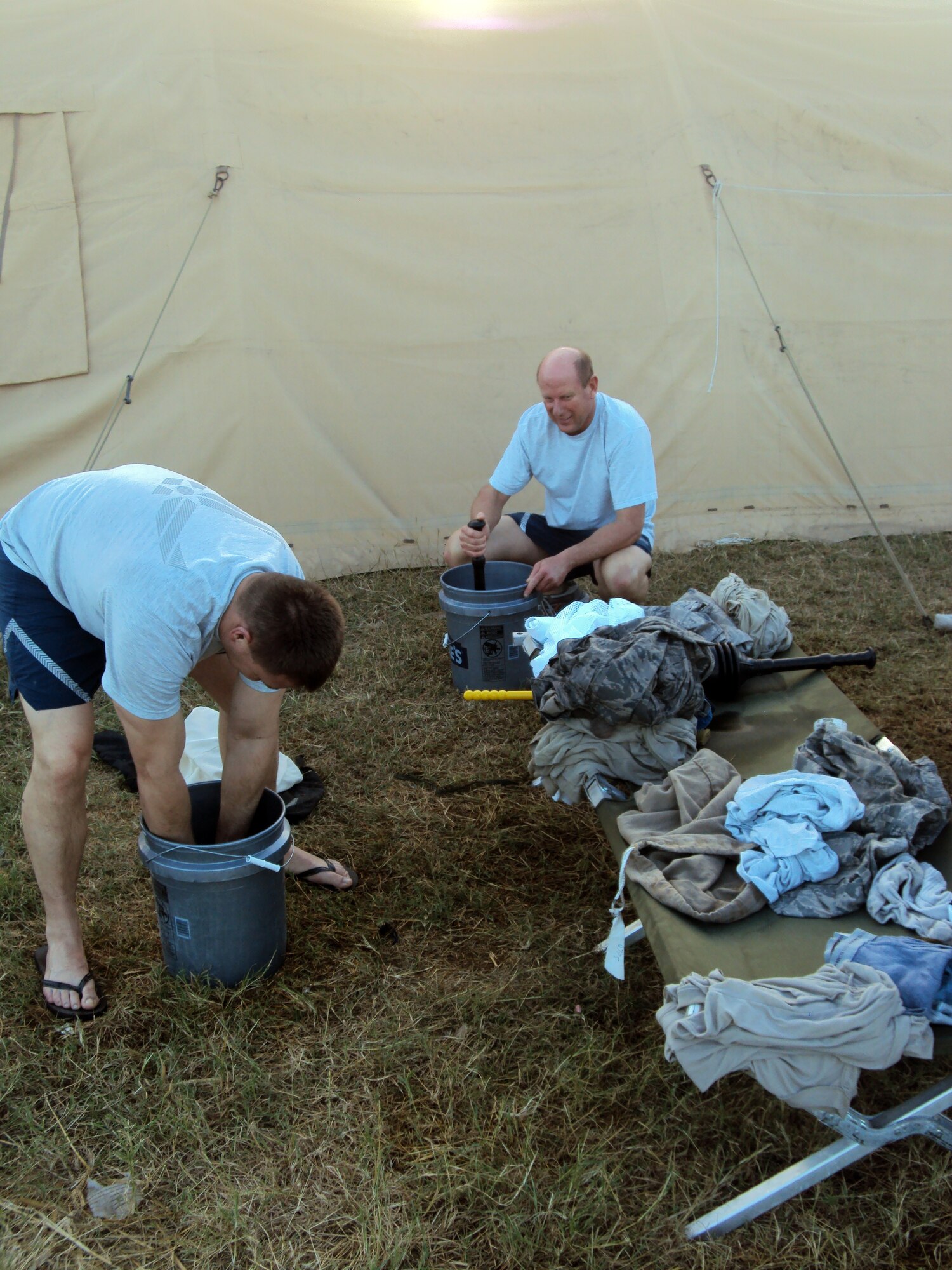 Tech. Sgt. Brent Barney and Tech. Sgt. Dennis Barton use plungers and their bare hands to clean clothes outside their temporary tent-residence in Port-au-Prince, Haiti. (Courtesy photo)