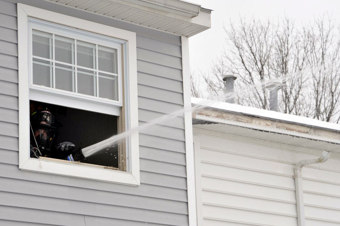 Colonel Steven Shepro, Joint Base Andrews/316th Wing commander, uses a 1 3/4 inches hand-line to hydraulically ventilate a house on Joint Base Andrews, Md., Feb. 23, 2010. Spraying water out of the window causes negative pressure, which sucks the smoke out of the building to increase visibility. Colonel Shepro was accompanied by his Airman "shadow," and together they worked with the 316th Civil Engineer Squadron fire department for the day. (U.S. Air Force photo by Airman 1st Class Perry Aston) (Released)