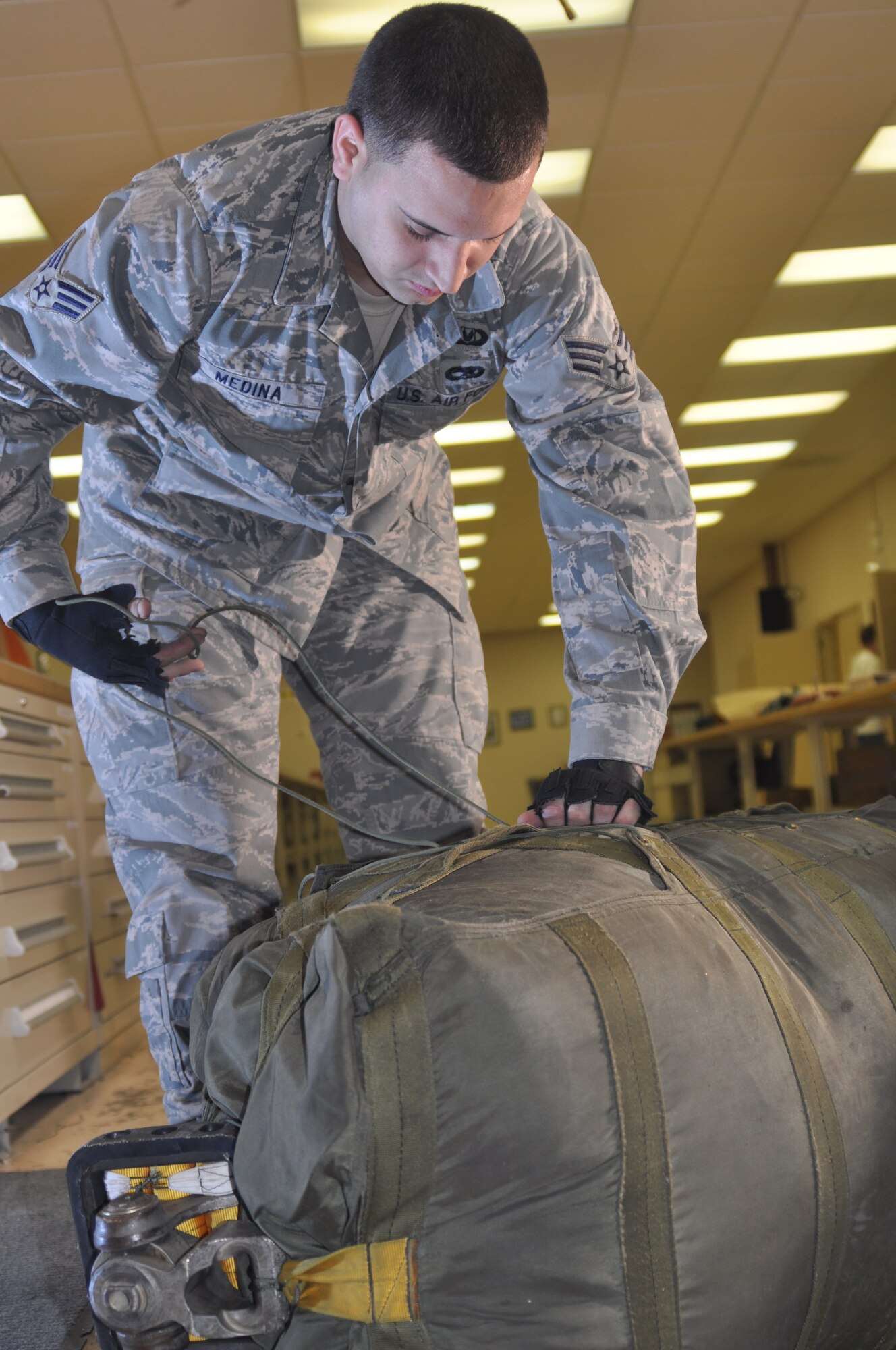 Senior Airman Xavier Medina, a Regular Air Force aircrew flight equipment journeyman attached to the 917th Wing at Barksdale Air Force Base, La., tugs at a series of strings in order to tighten and secure a B-52 Stratofortress parachute pack. Airman Medina, who is working at the 917th in support of Total Force Integration, packed the parachute while being filmed and photographed for an Air National Guard training video. (U.S. Air Force Photo/Senior Airman Crystal Marie Jordan)