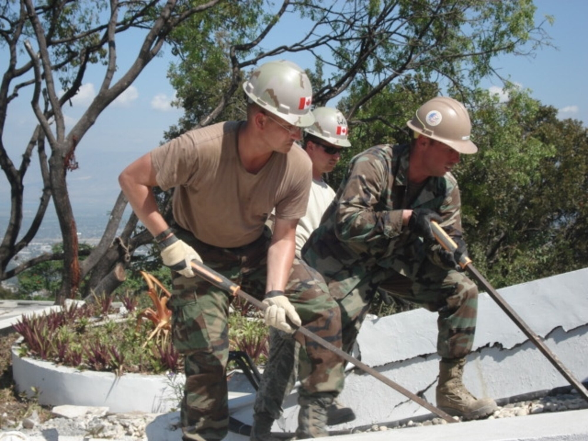 SCOTT AIR FORCE BASE, Ill. -- Master Sgt. Bradley Beaty, from Scott AFB, (forefront), works with a Navy Seebee and Canadian firefighters to clear material from a collapsed roof of a shopping area next to the Hotel Montana. He’s part of a 26-person Air Force firefighting team sent to Haiti to assist with protecting resources at the airfield and assist with recovery efforts. (Courtesy Photo)
