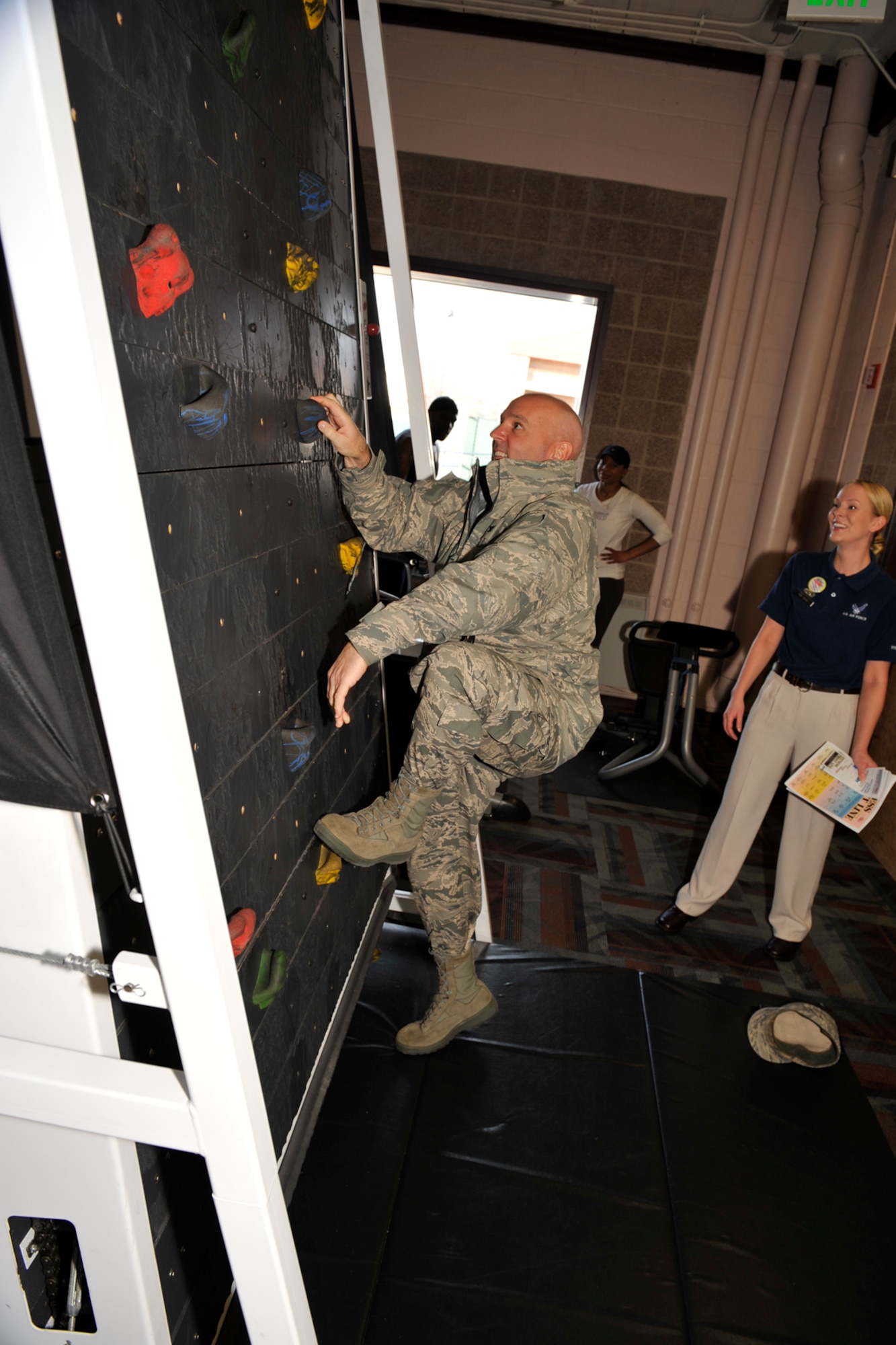 Col. Patrick Dunn, Headquarters Air Force Services Agency director of services directorate, attempts to scale the climbing wall Jan. 23 at the Peterson Fitness and Sports Center, Building 560, while Airman 1st Class Casey Mann, fitness specialist, looks on. The 21st Force Support Squadron earned the prestigious Curtis E. LeMay Award, naming the squadron the best service organization in the Air Force, officials announced Feb. 23.  Colonel Dunn and a six-member team visited the 21st Force Support Squadron programs before awarding the prestigious Curtis E. LeMay award for the best services organization. The Peterson Fitness and Sports Center is used by an average of 675,000 patrons every year. (U.S. Air Force photo/Robb Lingley)