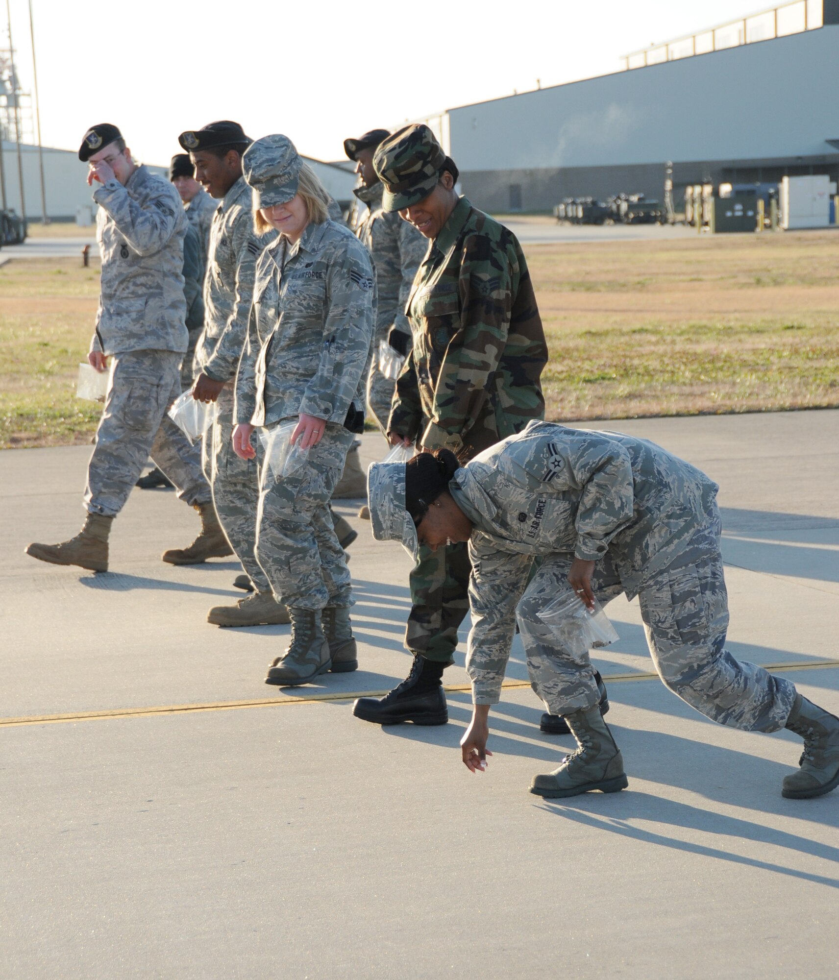 Airman 1st Class Tiffany Johnson, right, scoops up a piece of debris on the flightline during Friday’s FOD?walk. Watching are other members of the 81st Force Support Squadron, including Senior Airmen Kathryn Brown, center, and Iris Franklin.  (U.S. Air Force photo by Kemberly Groue)
