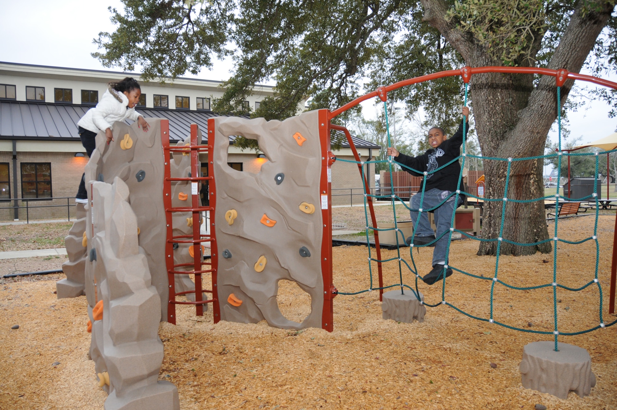 Summar Hughes, 8, scales the rock wall while her 9-year-old brother, Herman, climbs a net on the new youth center playground Tuesday.  The children’s parents are Tech. Sgt. Byron and LaToya Self, 81st Security Forces Squadron.  (U.S. Air Force photo by Kemberly Groue)