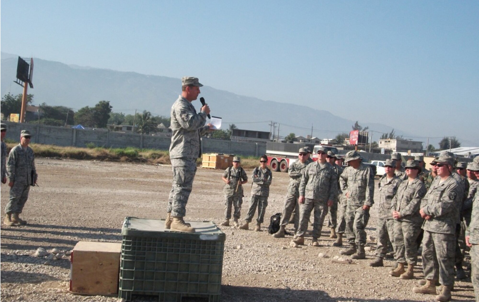 PORT AU PRINCE, Haiti -  Command Chief Master Sgt. Gerald Delebreau, 920th Rescue Wing Reserve Command Chief, works with what he has - a plastic box which he stands upon to address the troops.  This gathering in March 2010 of deployed Airmen is an exchange of information.  A daily ritual to ensure the deployed Airmen are equipped prior to their daily efforts to help the people of Haiti after their country was ravaged by an earthquake. (Courtesy photo)