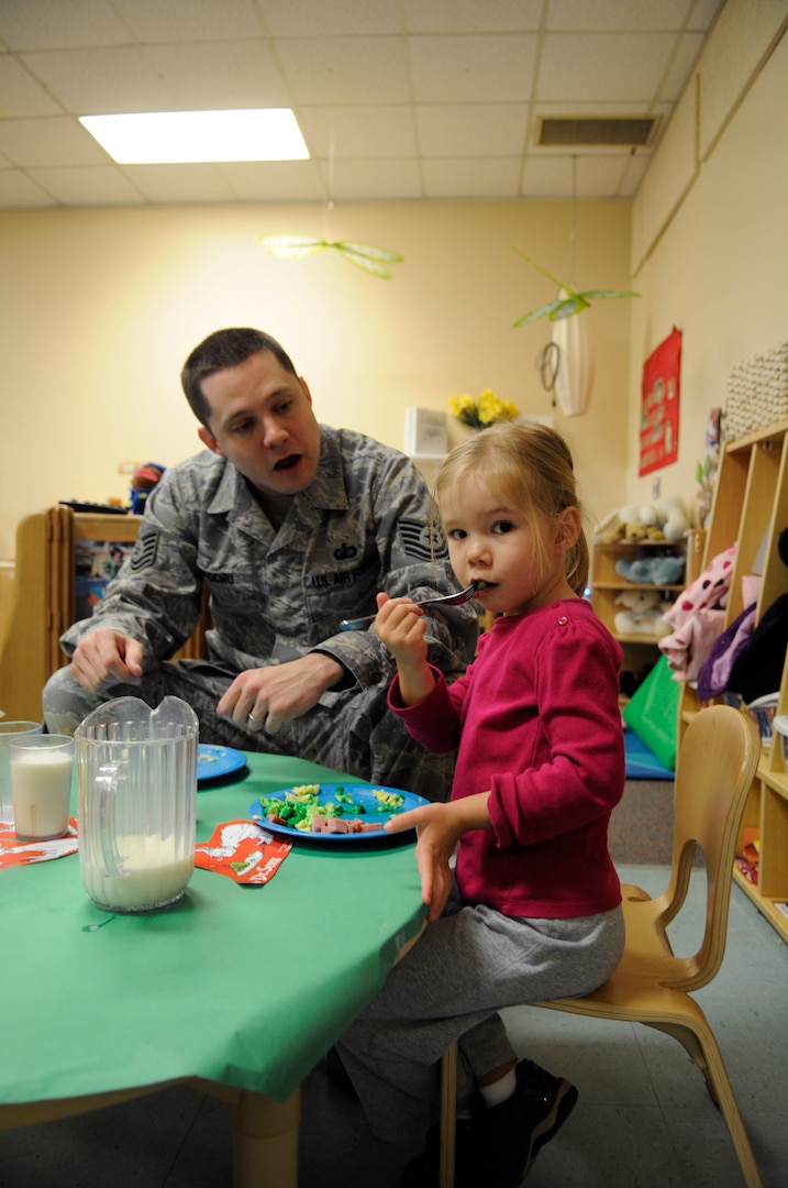 Tech. Sgt. Gilles Brochu, Air Education and Training Command, offers encourgement to daughter, Lauren, as she enjoys green eggs and ham on Dr. Suess' birthday at the Child Development Center at Randolph Air Force Base, TX. (U.S. Air Force Photo by Steve White)