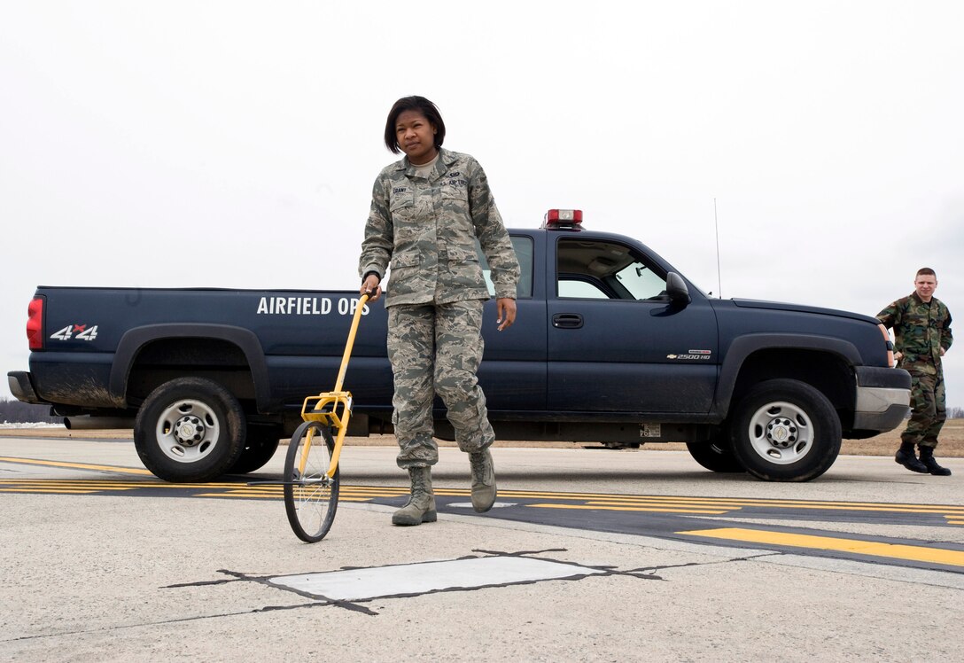 Airman 1st Class Mariah Grant, 316th Operations Support Squadron airfield management coordinator, uses a measuring wheel to verify location of visual flight rule holdlines on the flightline to ensure they are correctly annotated on the aircraft parking plan, as Senior Airman Steven Petrovic, 316 OSS airfield management coordinator, observes Tuesday morning. (U.S. Air Force photo/ Bobby Jones)