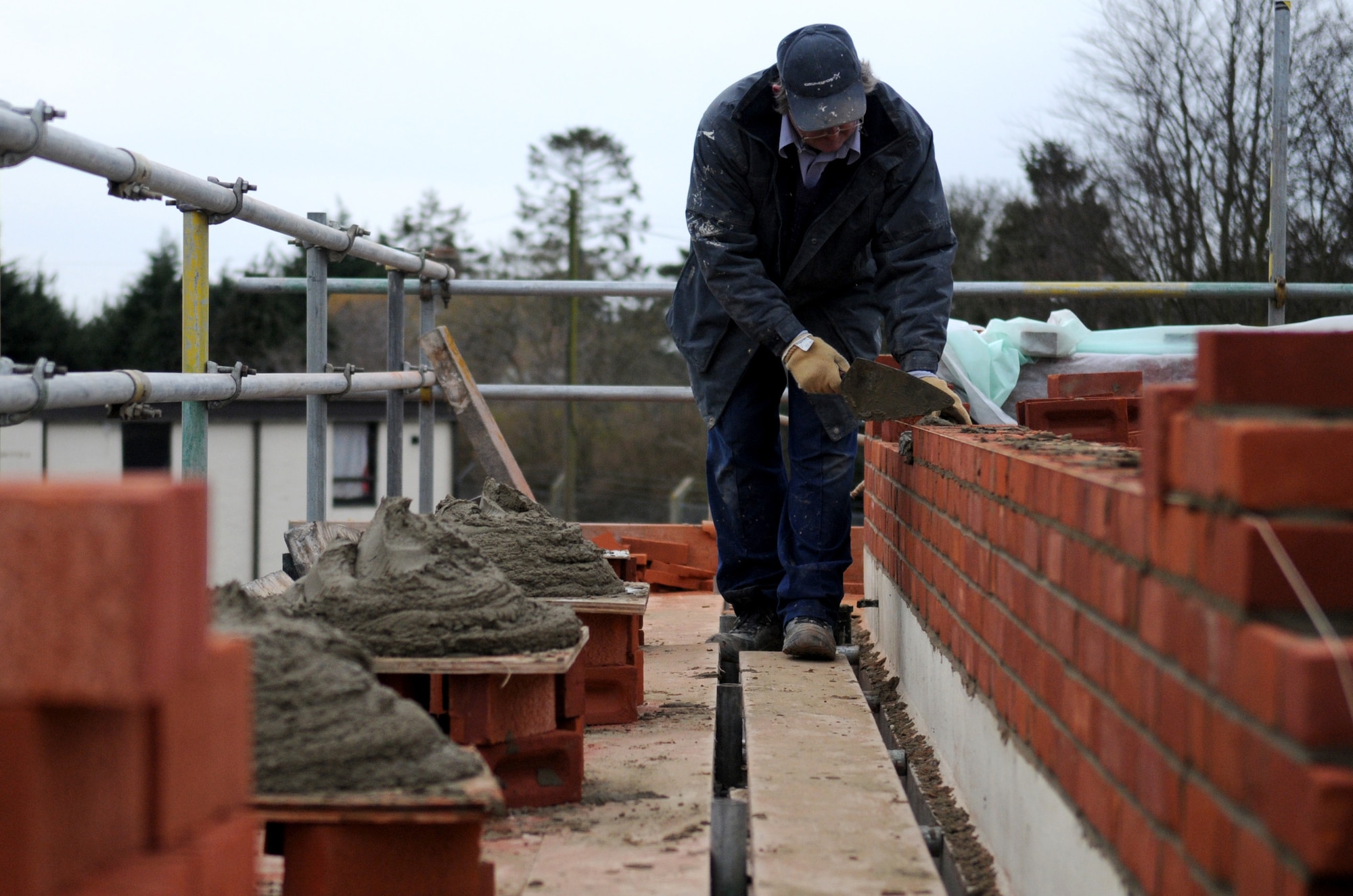 RAF MILDENHALL, England – Dave Garrett, a contracted mason worker, lays a new wall of bricks on top of Building 514 in a reroofing project March 3. This is one of several buildings in the area repaired due to deteriorated, damaged or worn material. The purpose of the project is to ensure the integrity of the building and safety of the occupants. (U.S. Air Force photo/ Staff Sgt. Jerry Fleshman)