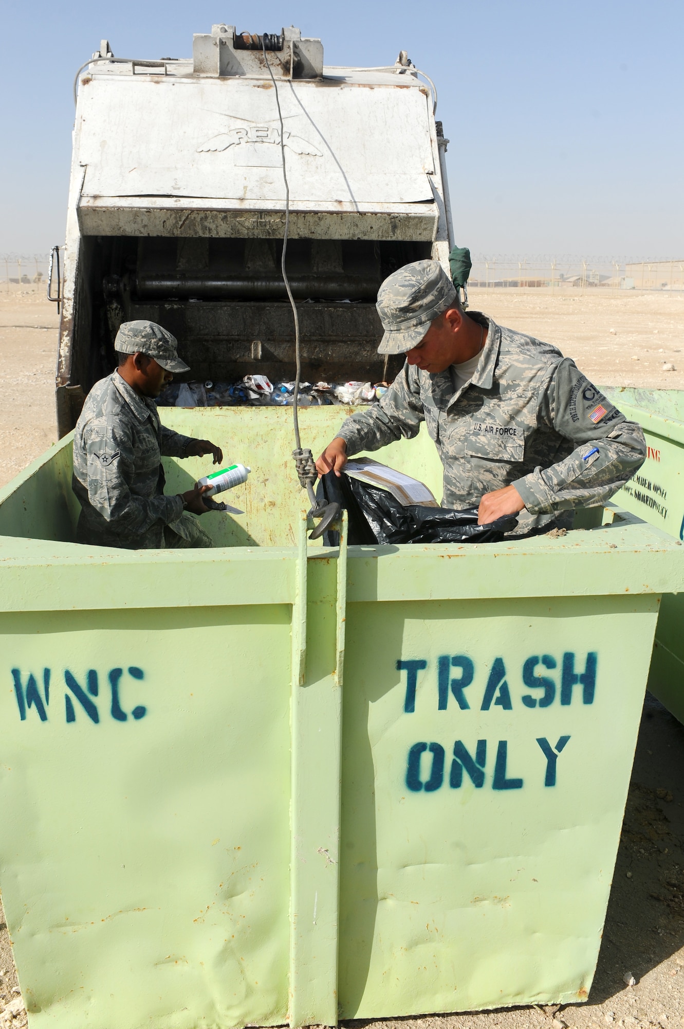 Airman Michael Bowens (left) and Airman 1st Class Ricky Shelton (right) search a dumpster for operations security violations at a non-disclosed Southwest Asia location March 3, 2010. The Airmen are deployed to the 379th Expeditionary Civil Engineer Squadron as security escorts. (U.S. Air Force photo by Senior Airman Kasey Zickmund)[RELEASED]