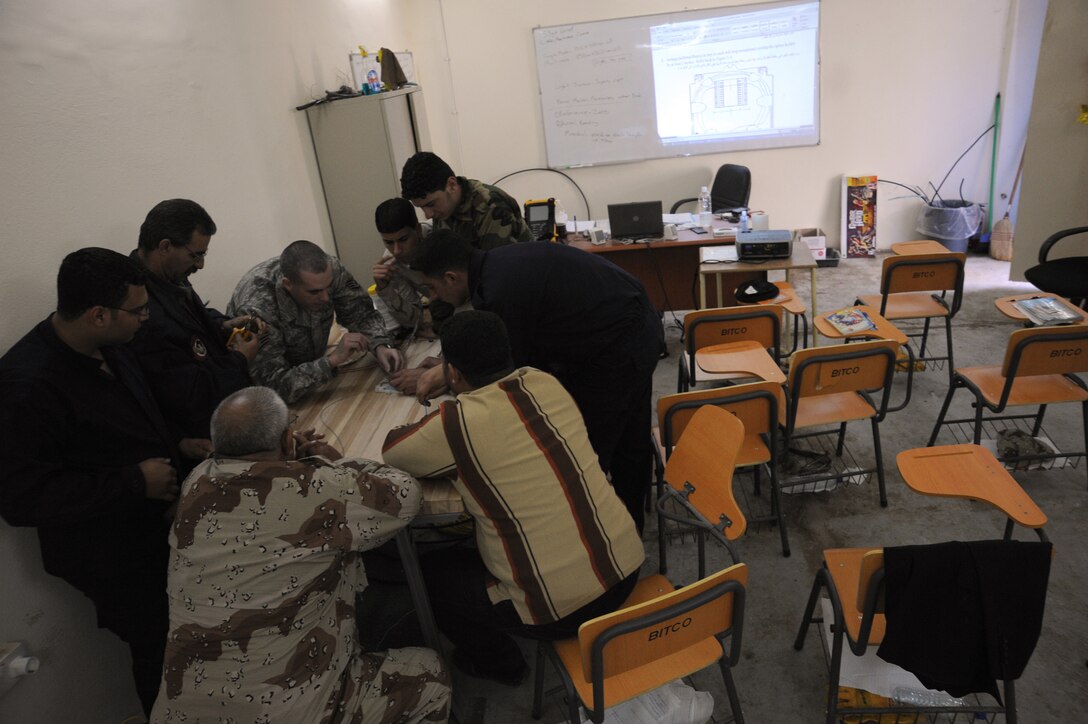 Air Force Staff Sgt. Gary Graf, 821st Expeditionary Training Squadron cable and antenna maintenance instructor, gathers his students around a table to closely teach them some of the aspects of fiber optics during class at Camp Taji, Iraq, Feb. 13, 2010. During this 42 day course the Iraqi military students learn about theories, splicing cable and the overall capabilities that fiber optics can bring in advancements. (U.S. Air Force photo/Master Sgt. Trish Bunting/Released)