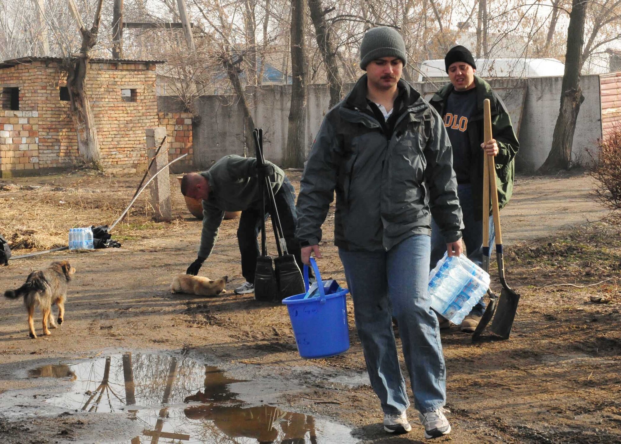 1st Lt. Nick Herr, Master Sgt. Dean Burlew, and Senior Airman Wesley Kliwinski bring supplies they need for cleaning and yard work up the driveway of a building that will soon be renovated to become the Crisis Center for Women in Bishkek, Kyrgyzstan, March 5. They are all Transit Center at Manas Airmen, and together with the Kyrgyz Congress of Women, they will help make the crisis center a place women can come for refuge. There will be a ceremony soon to officially begin the renovations. (U.S. Air Force photo/Staff Sgt. Carolyn Viss/released)