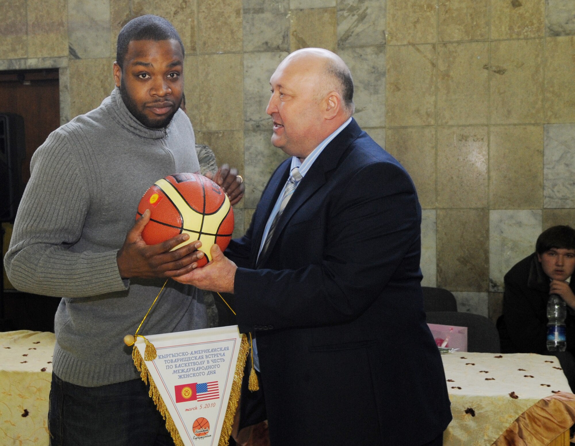 The Transit Center at Manas Women?s Basketball coach, Staff Sgt. Christopher Williams, accepts a commemorative basketball and banner from the vice president of the sports federation during the closing ceremony of the friendly basketball game against the Technical University at the Palace of Sport in Bishkek, Kyrgyzstan, March 5, 2010. The team participated in friendly game organized to unite the women in honor of International Women's Day. (U.S. Air Force photo/Senior Airman Nichelle Anderson/released)