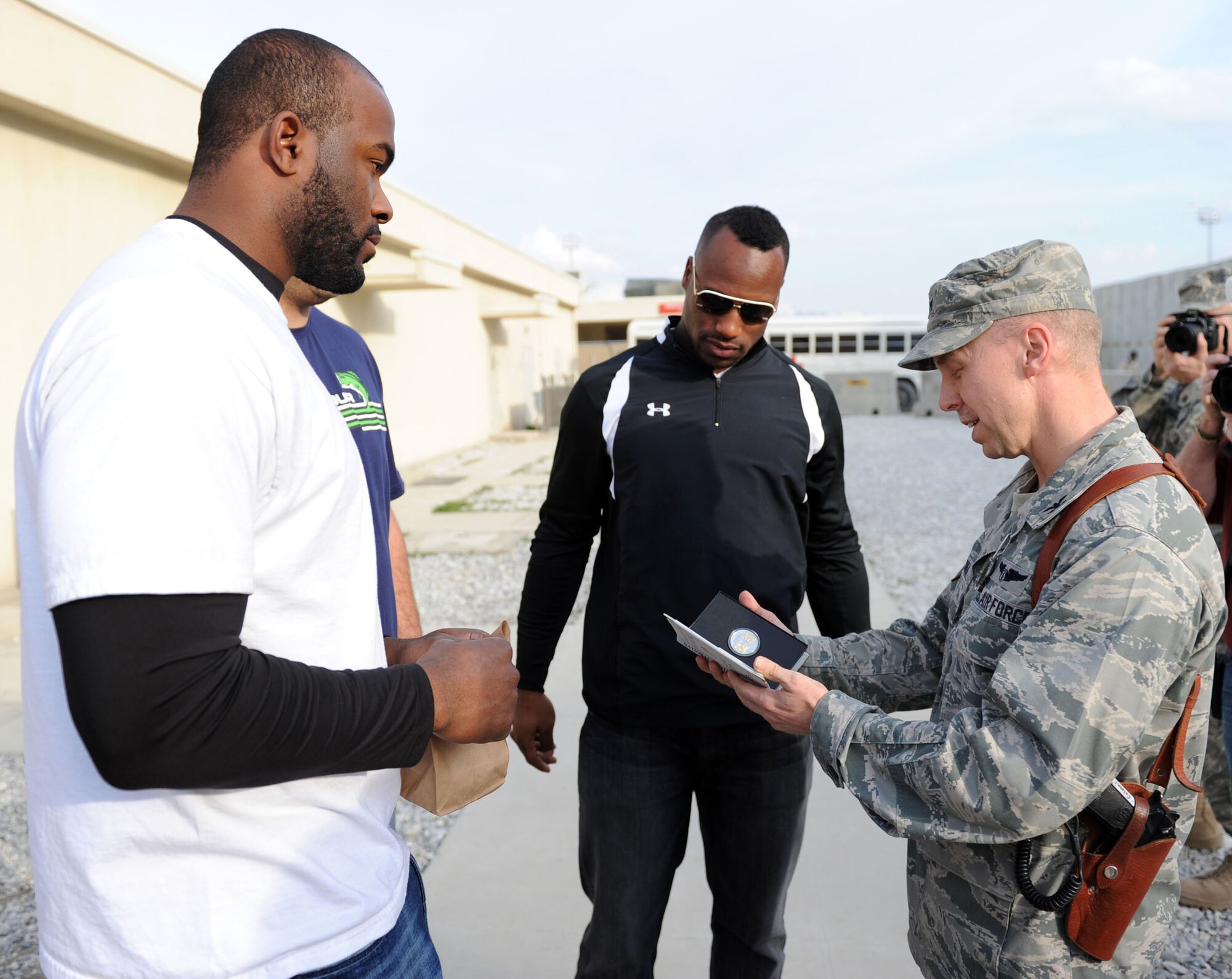 Col. Joseph Chozinski receives an official game day coin from Mario Williams of  the Houston Texans and Vernon Davis of the San Francisco 49ers during the National Football League players visit to the Craig Joint Theater Hospital March 5, 2010, at Bagram Airfield, Afghanistan. Colonel Chozinski is the 455th Expeditionary Medical Group/Task Force Medical commander. (U.S. Air Force photo/Staff Sgt. Richard Williams)