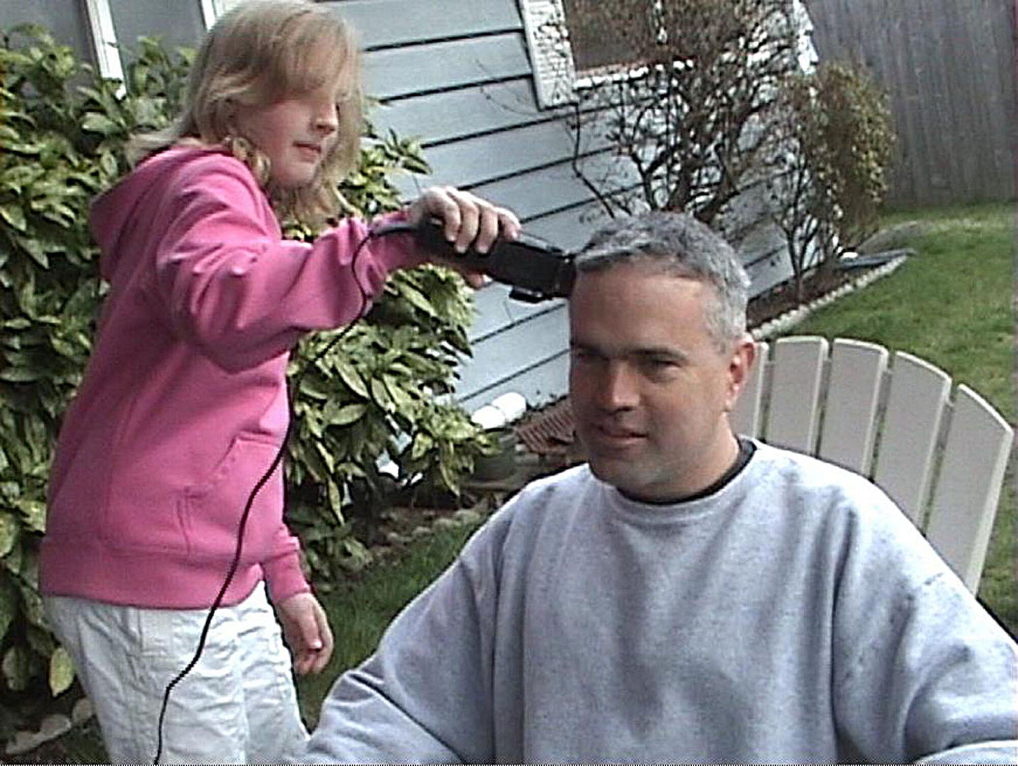 JOINT BASE LEWIS-MCCHORD, Wash., - Hannah Foster, left, takes hair clippers to her friend's father, Lt. Col. Joe Nauman, in a lighthearted approach to his hair loss due to chemotherapy. Colonel Nauman, a Reservist with the 97th Airlift Squadron, JBLM McChord Field, recently visited the doctor in New Zealand whom he credits with initiating the discovery of his illness. (Courtesy photo) 