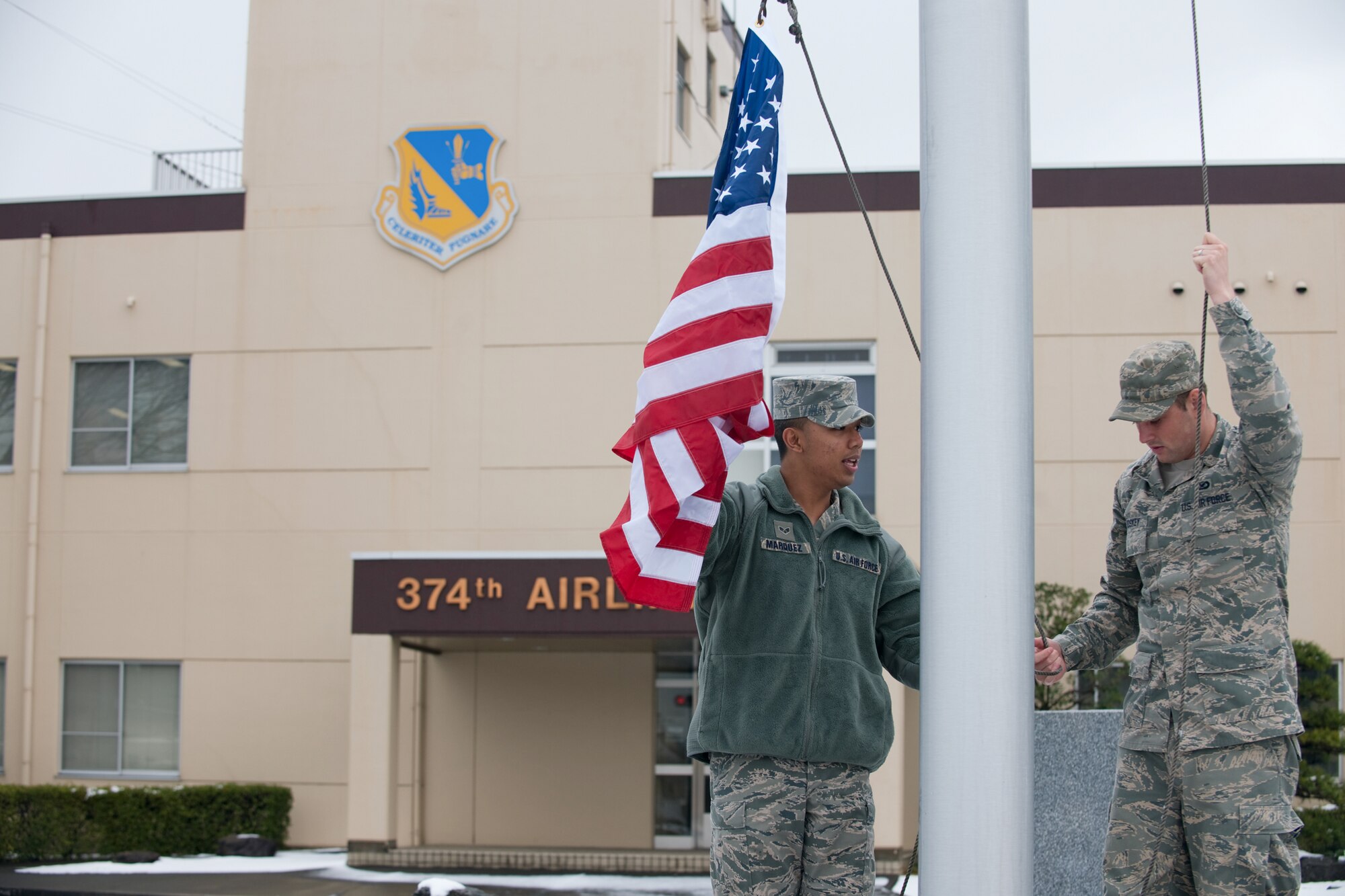 YOKOTA AIR BASE, Japan -- Senior Airman Mario Marquez and Airman 1st Class Devin Doskey, both from the  374th Airlift Wing, secure the American flag March 10. Airman Marquez  and Airman Doskey raised and lowered the flag for the base honor guard. The American flag is presented to Airmen upon retirement and symbolizes their service to the United States. (U.S. Air Force photo/Osakabe Yasuo)