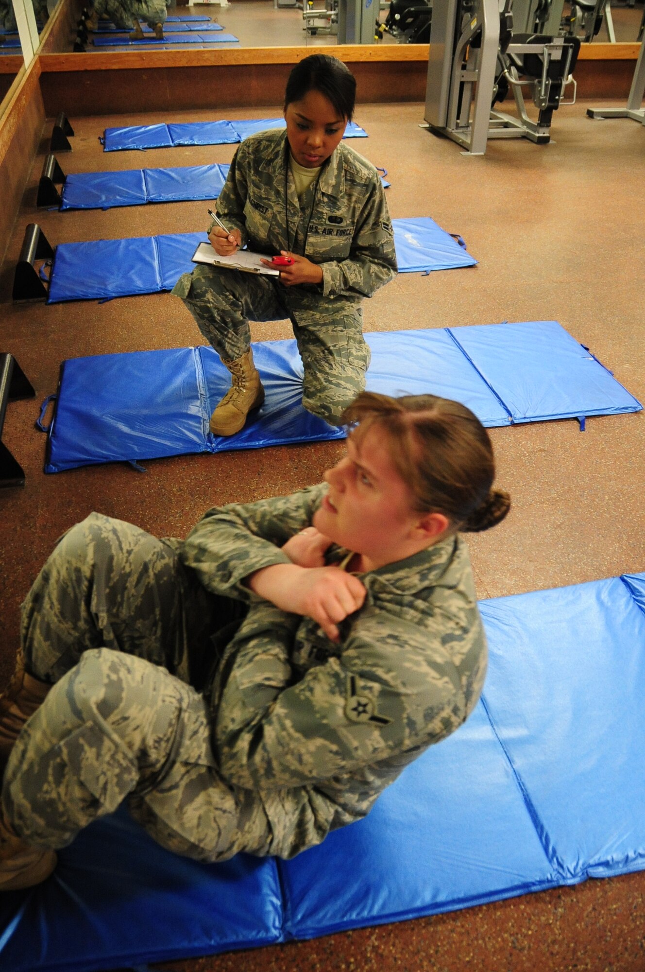 ELLSWORTH AIR FORCE BASE, S.D. -- (Front to back) Airman Kaitlin Walker, 28th Bomb Wing radio and television broadcaster, endures as many sit-ups as she can in two minutes while Airman 1st Class Elimae Gilchrist, 28th Force Support Squadron fitness specialist, keeps track of her time and number of sit-ups during a fitness assessment, March 9.  The fitness assessment both tests the individual’s fitness level and provides a benchmark for developing a personalized fitness program. (U.S. Air Force photo/Airman 1st Class Anthony Sanchelli)
