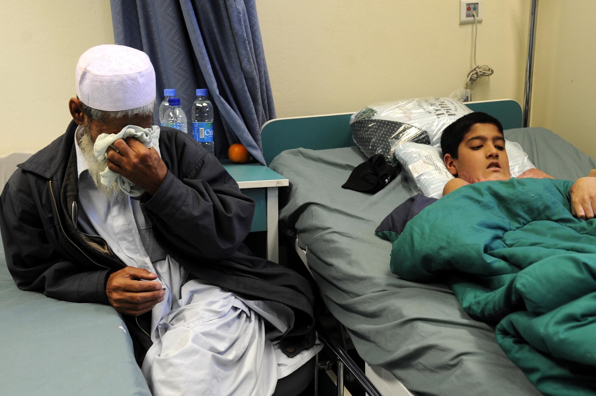 Abdul Ghafer, father, wipes his tears next to his son, Abdul Rahman, as they wait for the operation to begin March 1 at the Kandahar Regional Military Hospital.  Abdul Rahman has severe burns to his chest and neck after a cooking incident.  (U.S. Air Force photo by Senior Airman Nancy Hooks/Released)