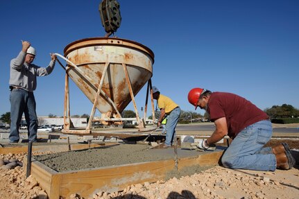 Bill Farrow positions a bucket filled with cement over a form while Bobby Pogue smoothes out the newly poured concrete during the replacement of the Randolph Field letters facing Washington Circle March 11 Mr. Farrow and Mr. Pogue are cement finishers with the 902nd Civil Engineer Squadron. (U.S. Air Force photo by Steve Thurow)