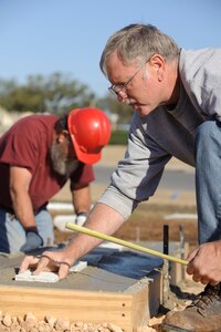 Bill Farrow and Bobby Pogue, 902nd Civil Engineer Squadron cement finishers, align a row of bricks being used to add texture to a freshly -poured concrete letter during the replacement of the Randolph Field letters facing Washington Circle March 11. (U.S. Air Force photo by Steve Thurow)