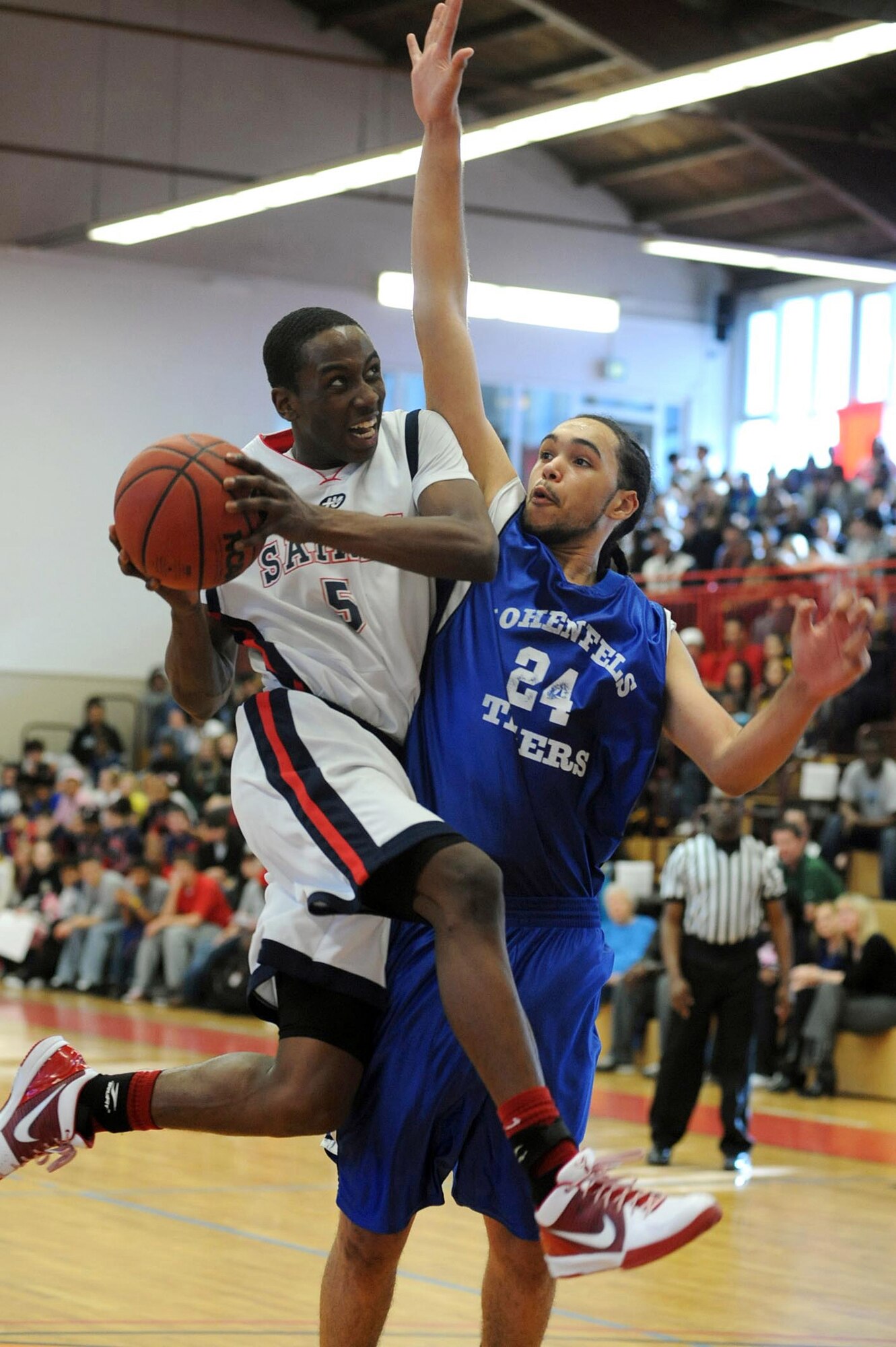 Aviano's Jamal Tuck sails toward the basket and Jordan Gaddy of Hohenfels in the Division II final at the DODDS-Europe basketball championships in Mannheim, Germany, on Feb. 27th, 2010.  Defending champion Aviano repeated with a 49-38 win.  (Photos by Michael Abrams.  Used with permission from the Stars and Stripes.  ? 2010 Stars and Stripes.)  