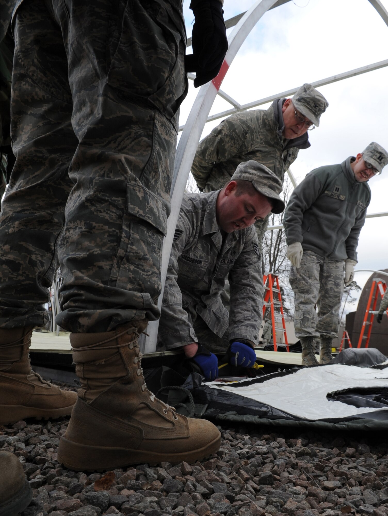 U.S. Air Force Staff. Sgt. Richard Jacobson, School of Aerospace Medicine instructor and public health technician, from Brooks City-Base, Texas, demonstrates the proper way to tie down tarps siding for a tent structure during the tent build up portion of the Expeditionary Medical Support (EMEDS) Mobile Course, Ramstein Air Base, Germany, March 15, 2010. The EMEDS course teaches and evaluates corps specific field situations as well as offers updates in Air Force Medical Service concept of operations and doctrine.  It also teaches setup and packing out of a field EMEDS compound, deployed operations, field medical, nursing and operational support equipment proficiency, field exercises to both emphasize and evaluate learning of concepts taught. (U.S. Air Force photo by Airman 1st Class Caleb Pierce)