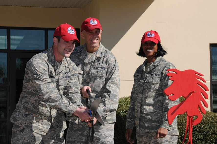 Col.Timothy Lamb (center), commander of the 567th Red Horse Squadron is assisted by 2nd Lt. Terrance Mathieu during the ribbon cutting ceremony for Red Horse Squadron's new building here in early March.  Squadron members showed their enthusiasm with a spirted shout of "to the horse" after the ribbon dropped. (U.S. Air Force photo by TSgt. Scotty Sweatt, 916ARW/PA)