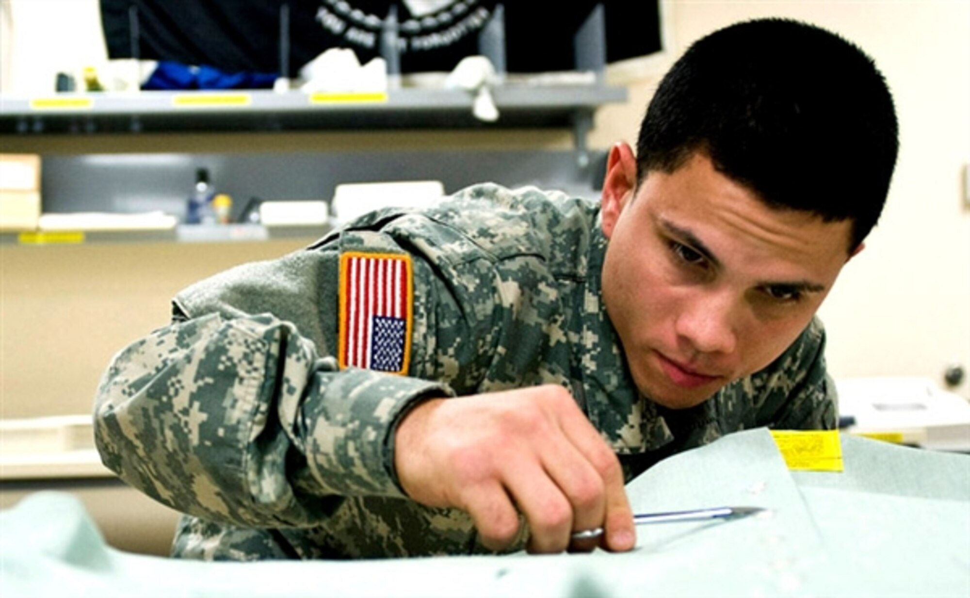 Army Spc. Xavier Gonzalez snips a thread off of a uniform shirt at the uniform shop of the Air Force Mortuary Affairs Operations Center at Dover Air Force Base, Del. Gonzalez prepares uniforms for fallen Soldiers’ remains. (U.S. Air Force photo)  
