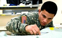 Army Spc. Xavier Gonzalez snips a thread off of a uniform shirt at the uniform shop of the Air Force Mortuary Affairs Operations Center at Dover Air Force Base, Del. Gonzalez prepares uniforms for fallen Soldiers’ remains. (U.S. Air Force photo)  
