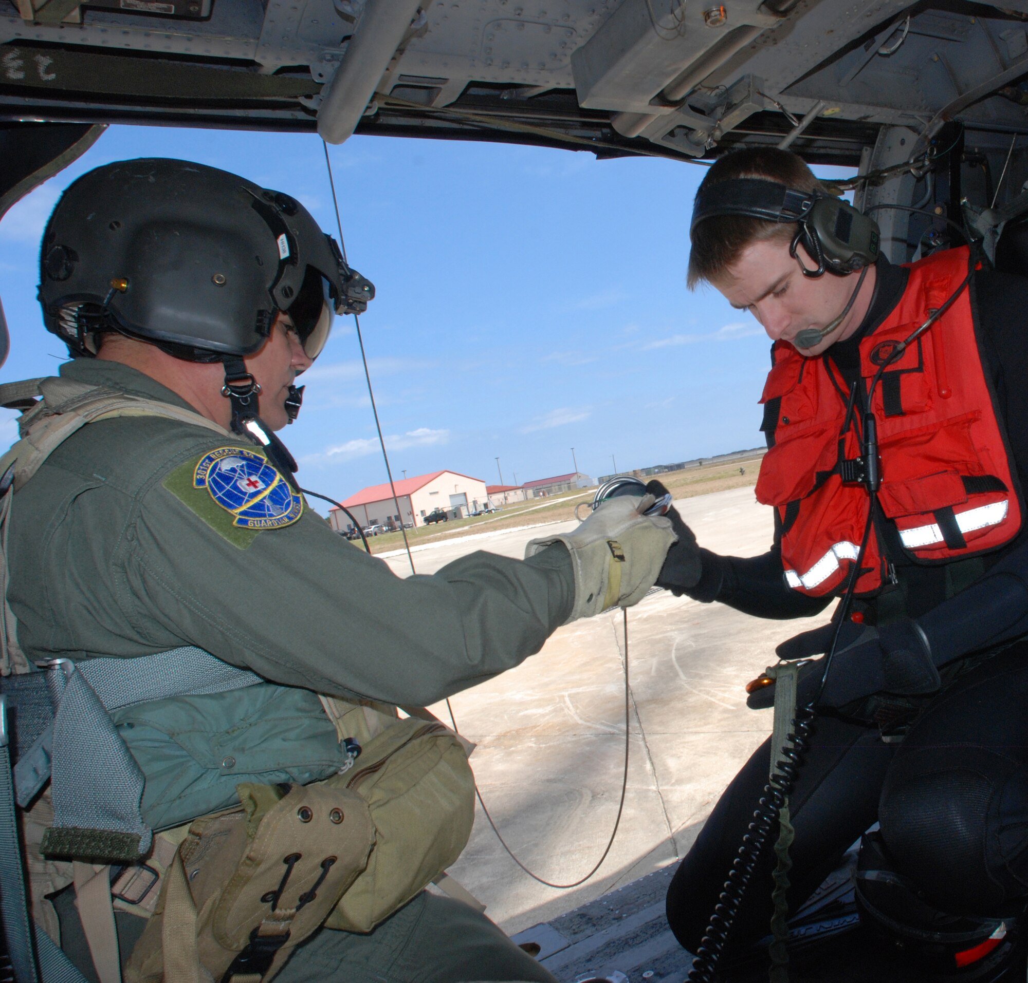 PATRICK AIR FORCE BASE, Fla. - Air Force Reserve Chief Master Sgt. Lazaro Ibarra, helicopter flight engineer, 920th Rescue Wing here, hands a hoisting cable to Master Sgt. Josiah Blanton, an Air Force Reserve Pararescueman (PJ) from the 304th Rescue Squadron base at Portland, Ore. The 304th RQS is a geographically separated unit (GSU) of the 920th RQW - they fall unter the 920th's jurisdiction but are stationed on the West Coast. For the PJs and helicopter crews, training together becomes important to keep camaraderie between the different crews and the different terrain is essential for real-world rescue scenarios. (U.S. Air Force photo/Staff Sgt. Leslie Kraushaar)