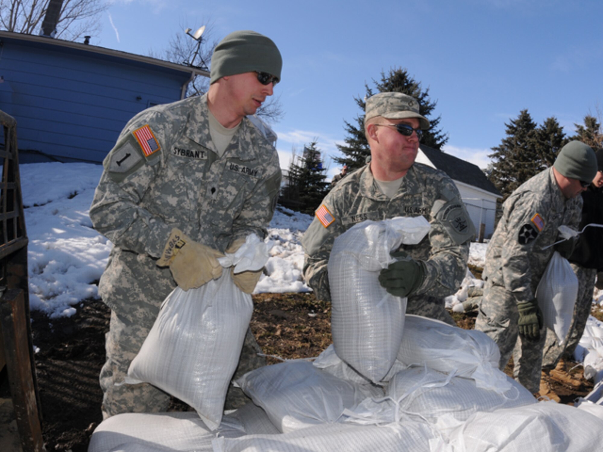 Spc. Tim Sybrant, of the 817th Engineer Sapper Company (Jamestown, N.D.), left, passes sandbags to Pfc. Scott Ness, of the 188th Engineer Company (Wahpeton, N.D.), March 17, in the backyard of Konny Zins and her husband, Sgt. Darin Zins, who is currently deployed to Kosovo and can do little more than empathize with his family during Skype calls from half a world away. He serves with the 231st Maneuver Task Force, part of the NATO peacekeeping forces in Kosovo Force 12. The Soldiers are building a sandbag flood barrier to hold back rising water from the Sheyenne River. (DoD photo by Senior Master Sgt. David H. Lipp) (Released)