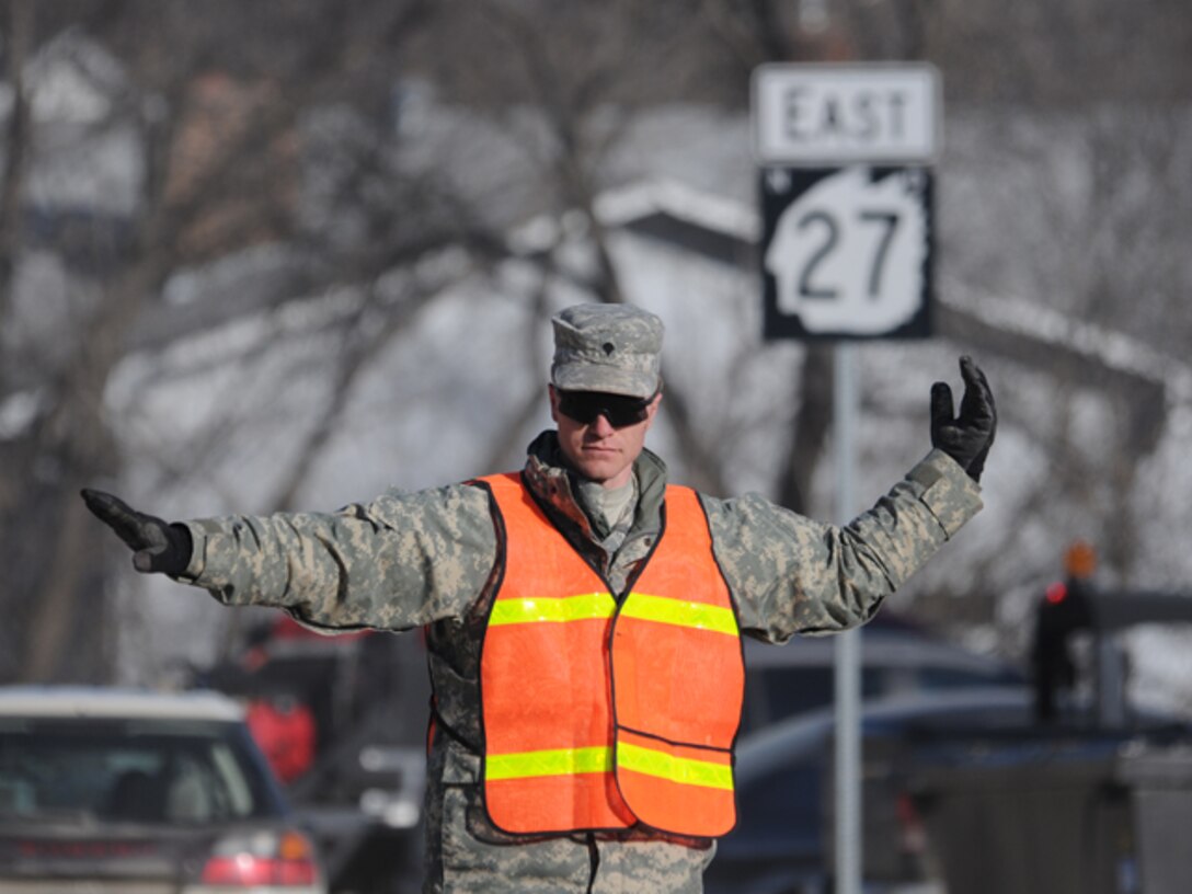 Spc. Danny Gross, of the 191st Military Police Company, directs traffic at a busy intersection March 17 in Lisbon, N.D.  Gross, of Enderlin, N.D., is operating a North Dakota National Guard traffic control point (TCP) in order to allow dump trucks carrying dike building clay to arrive at flood fighting locations in a timely manner.