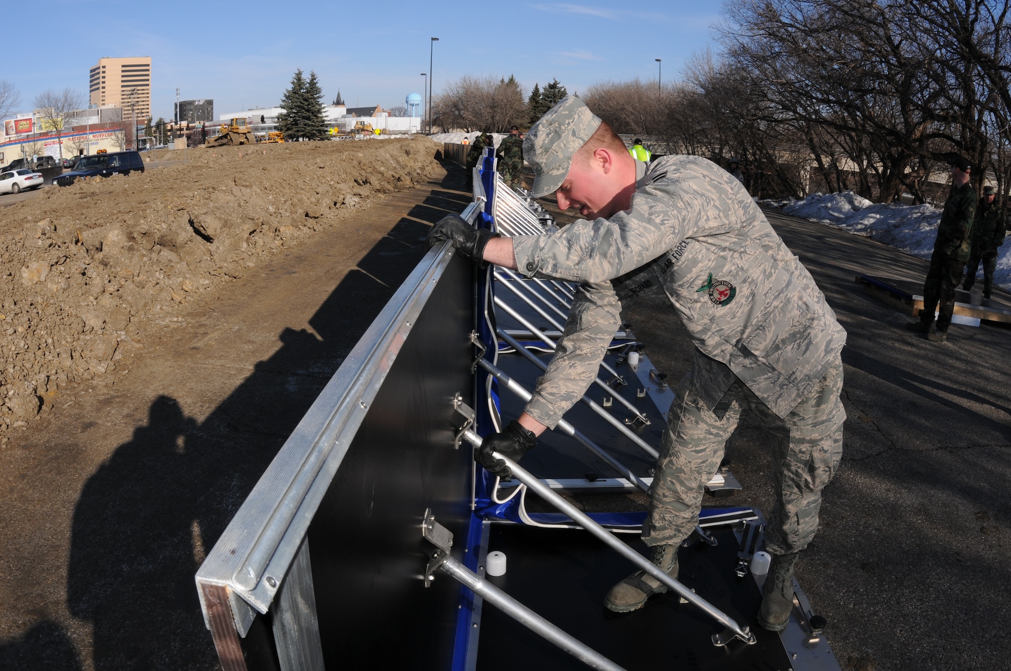 Airman 1st Class Casey Pritchard, of the 119th Civil Engineer Squadron, assembles a section of AquaFence March 17 near NP Avenue in Fargo, N.D. The fence is being installed by the North Dakota Air National Guard as a test flood barrier for the City of Fargo to see if it might be effective for use in future flood protection.  (DoD photo by Senior Master Sgt. David H. Lipp) (Released)