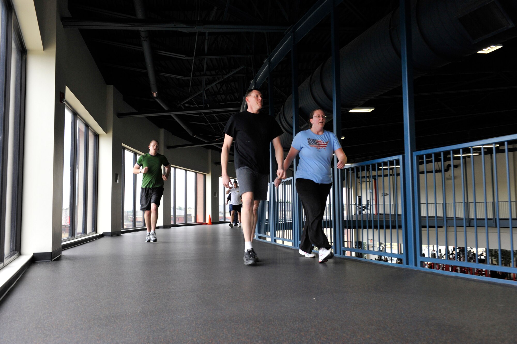 Staff Sgt. Matt Zorc, 311th Training Squadron military language instructor, jogs as Maj. Scott Lawson, 62nd Airlift Squadron pilot instructor, and his wife, Sharon, cool down after a run at the fitness center in the indoor track upstairs. The indoor track is available as an alternative when bad weather doesn't allow people to exercise outdoors.  (U.S. Air Force photo by Senior Airman Christine Clark)