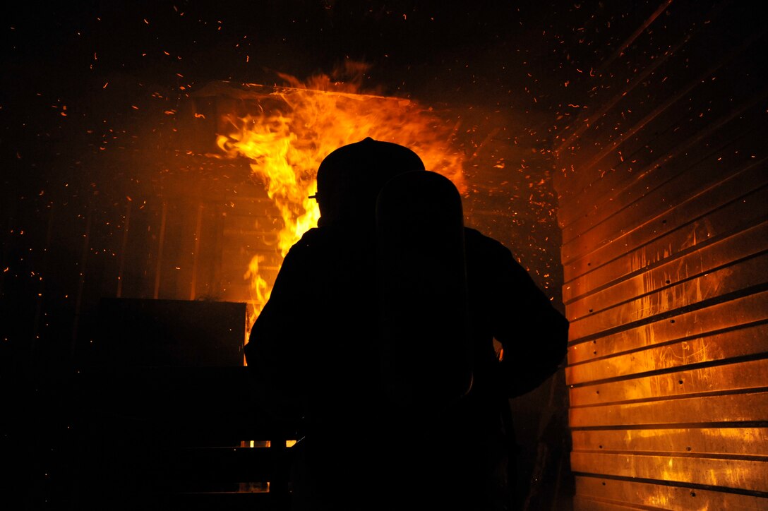 Joseph Thompson, 316th Civil Engineer Squadron fire protection assistant chief of operations throws excelsior on burning pallets during live fire training March 5, 2010, at Joint Base Andrews Md. Live fire training is a necessary and indispensable tool for 316?th CES firefighters. Giving the firefighters the ability to experience heat and flames from a structure fire, but in a controlled environment. (U.S. Air Force photo by Airman 1st Class Perry Aston) (Released)